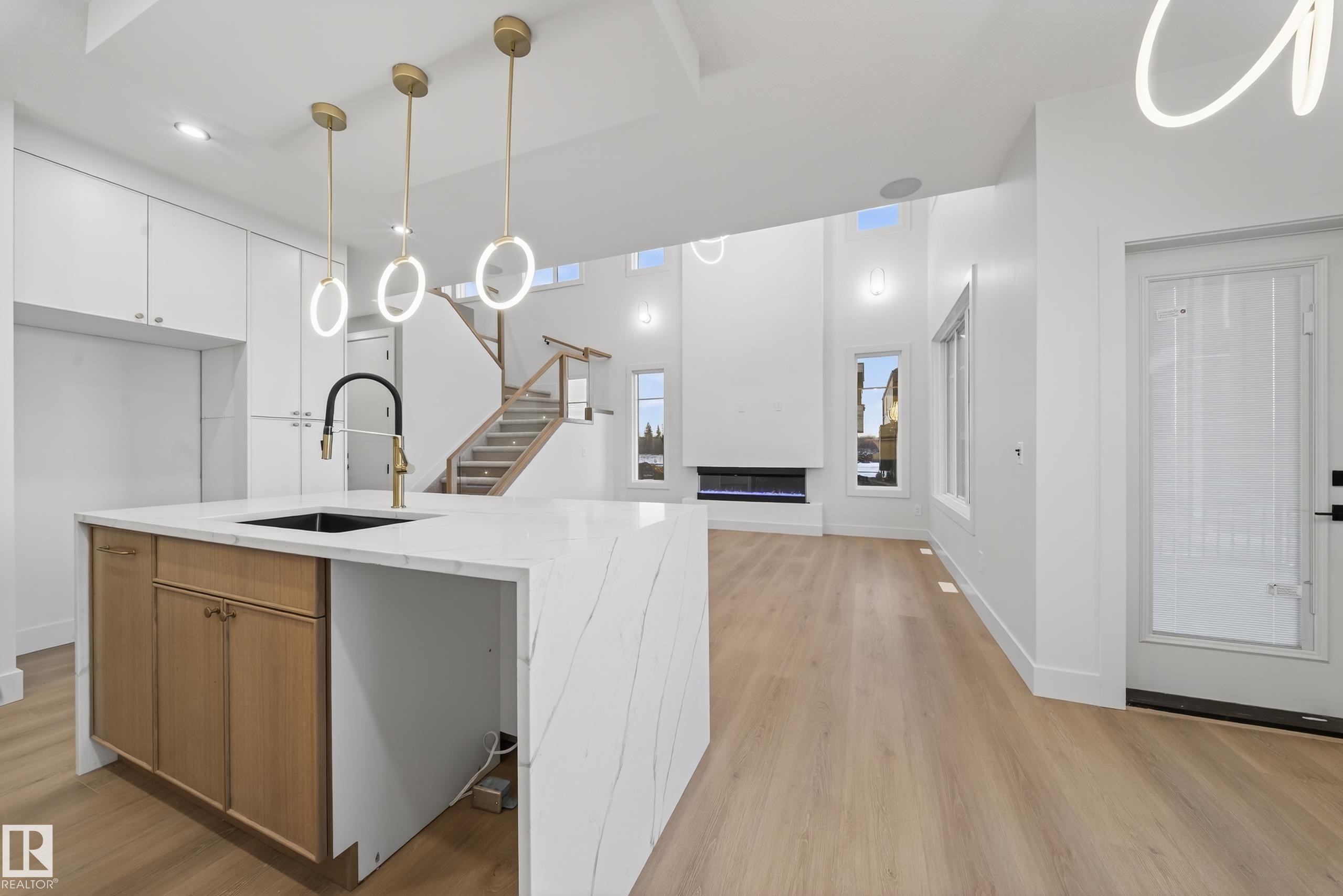 Kitchen with hanging light fixtures, light wood-style flooring, open floor plan, light stone countertops, and modern cabinets - 8924 Mayday Way, Edmonton, AB