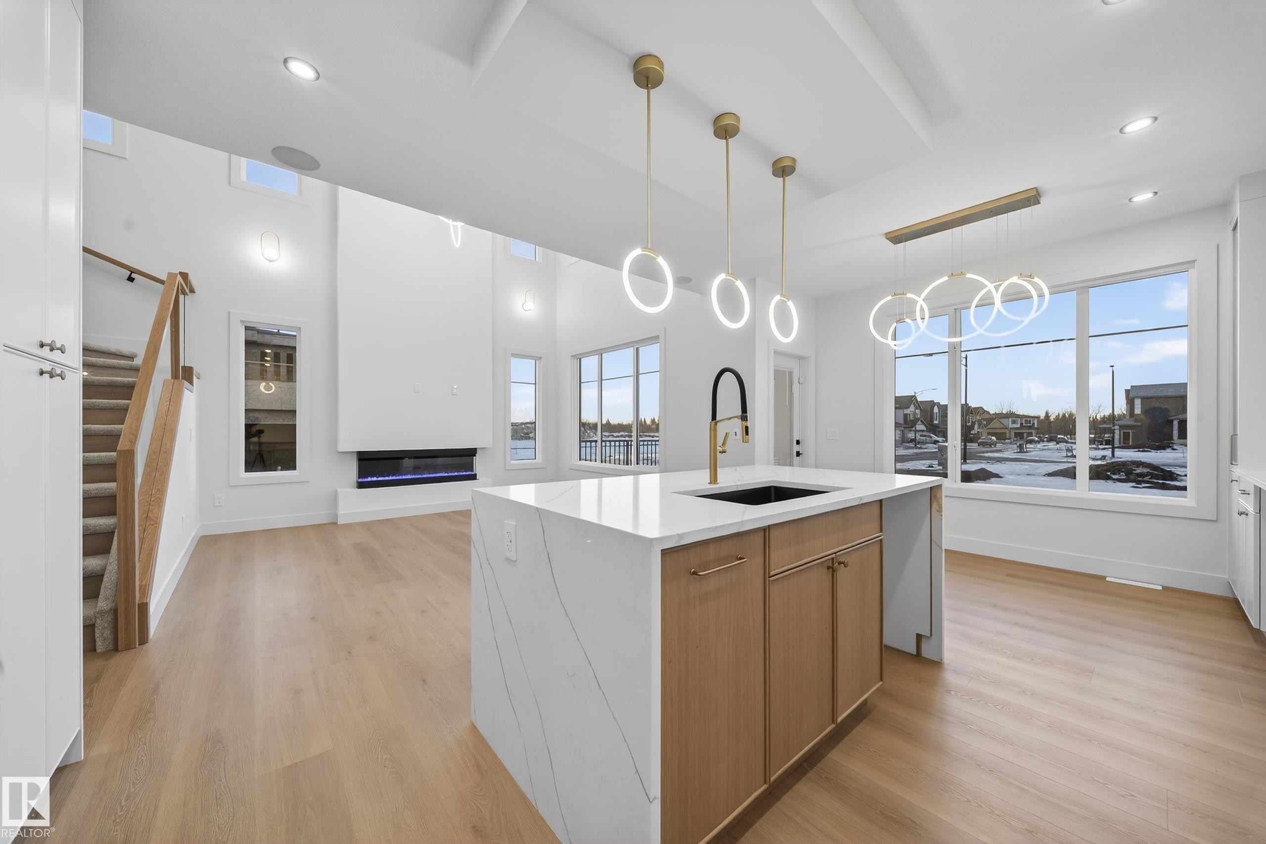 Kitchen with light stone counters, decorative light fixtures, light wood-style floors, a center island with sink, and open floor plan - 8924 Mayday Way, Edmonton, AB