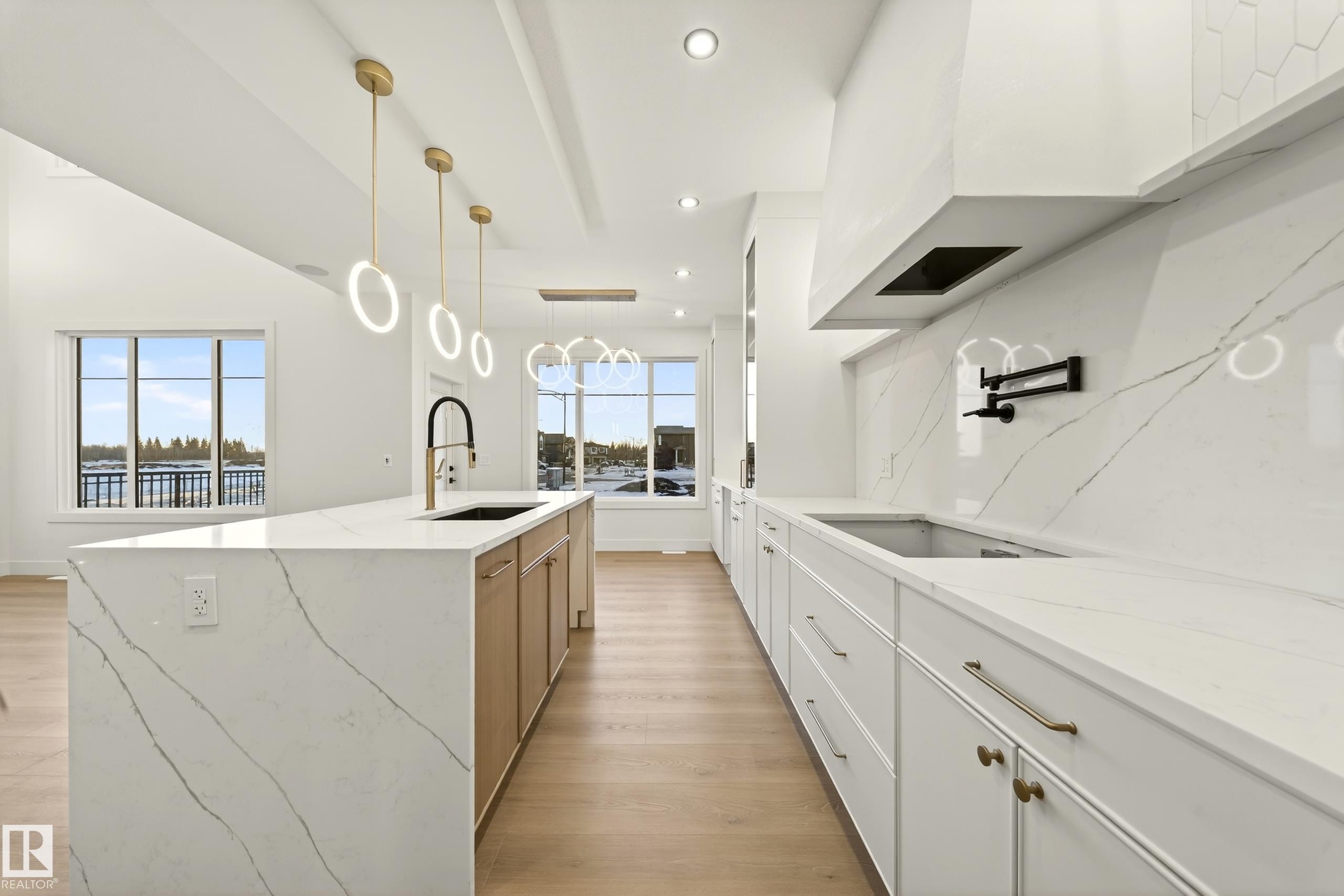 Two tone kitchen with two tone cabinetry, light stone countertops, light wood-type flooring, a kitchen island with sink, and hanging light fixtures - 8924 Mayday Way, Edmonton, AB