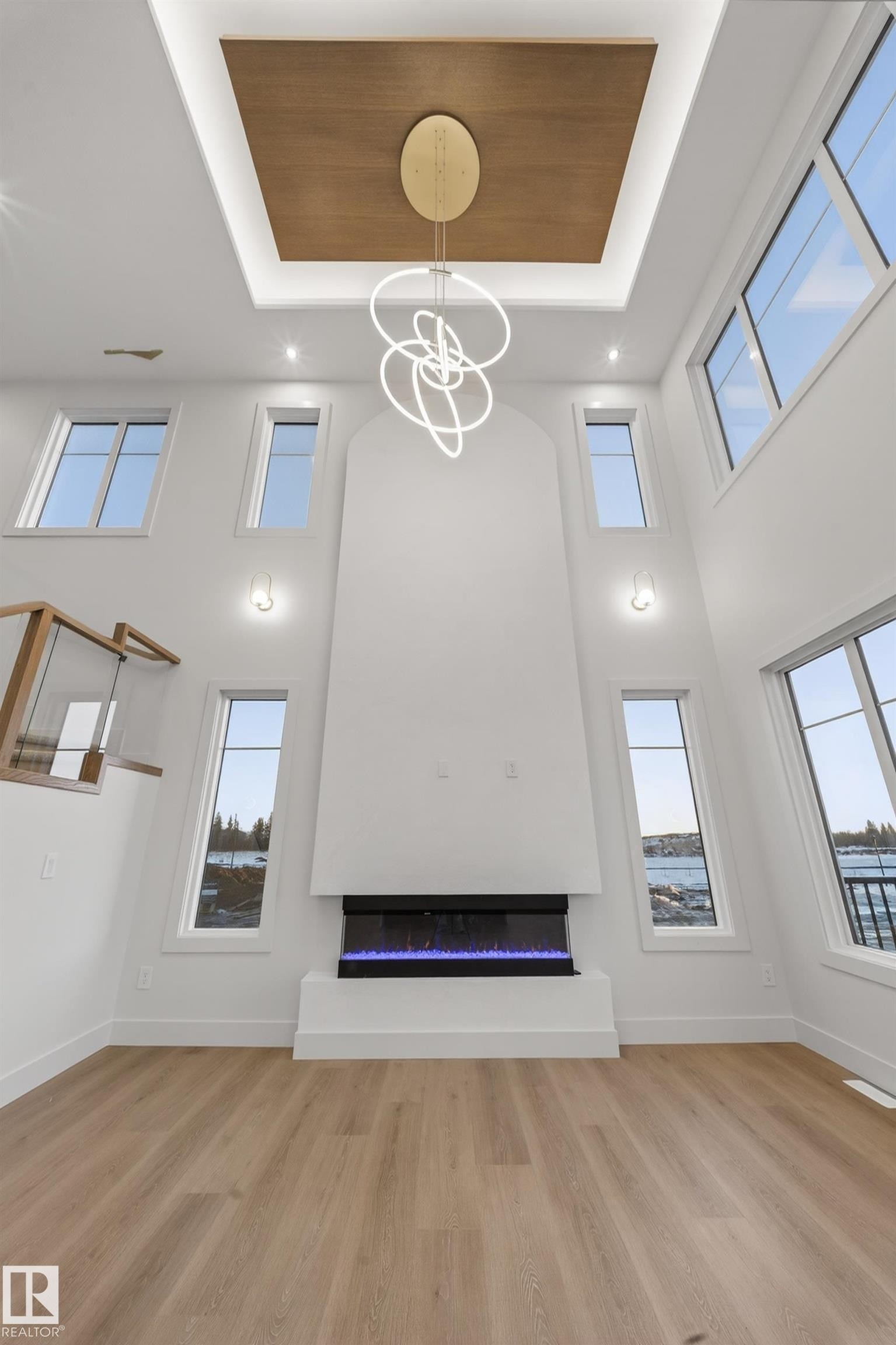 Unfurnished living room with a high tray ceiling, a glass covered fireplace, a chandelier, light wood-style floors, and plenty of natural light - 8924 Mayday Way, Edmonton, AB