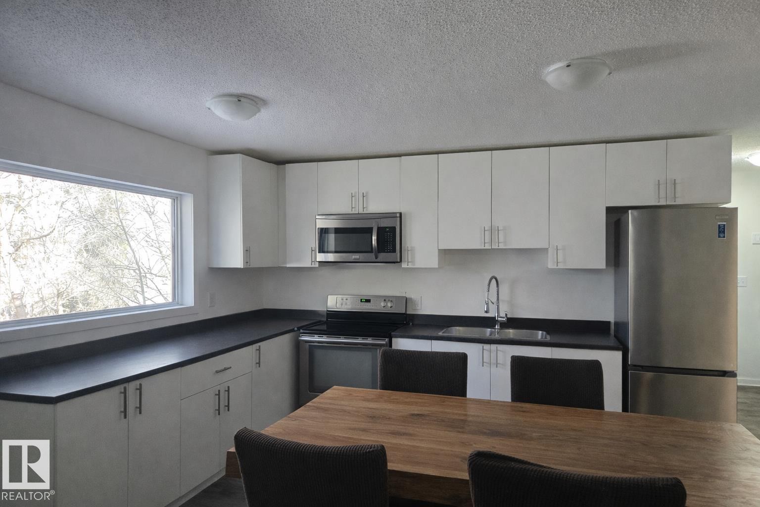 Kitchen with dark countertops, stainless steel appliances, white cabinetry, and a textured ceiling - 4513 53 Avenue, Wetaskiwin, AB - Indoor Photo Showing Kitchen