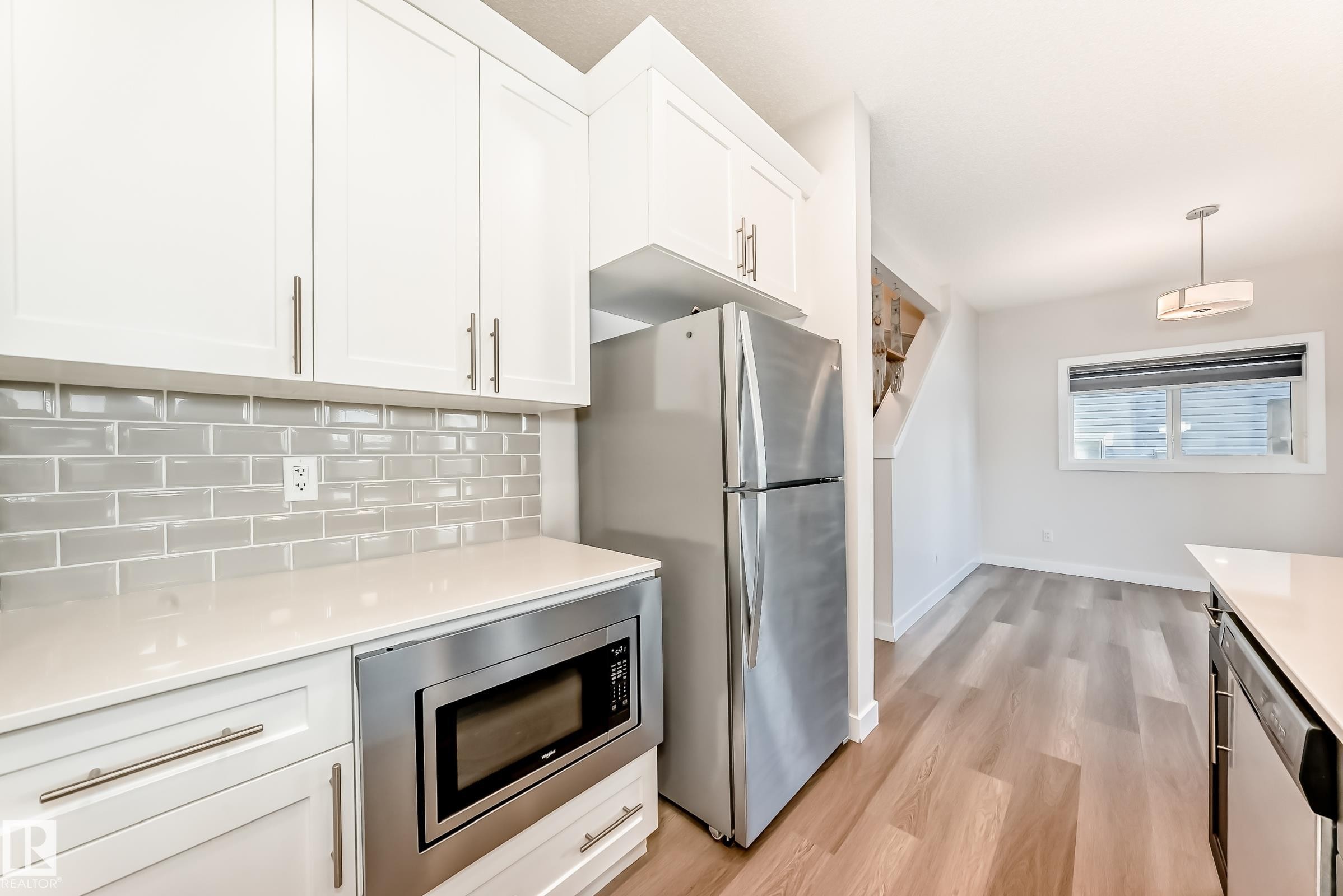 Kitchen featuring stainless steel appliances, hanging light fixtures, white cabinets, light wood-type flooring, and backsplash - 17926 62A Street, Edmonton, AB - Indoor Photo Showing Kitchen