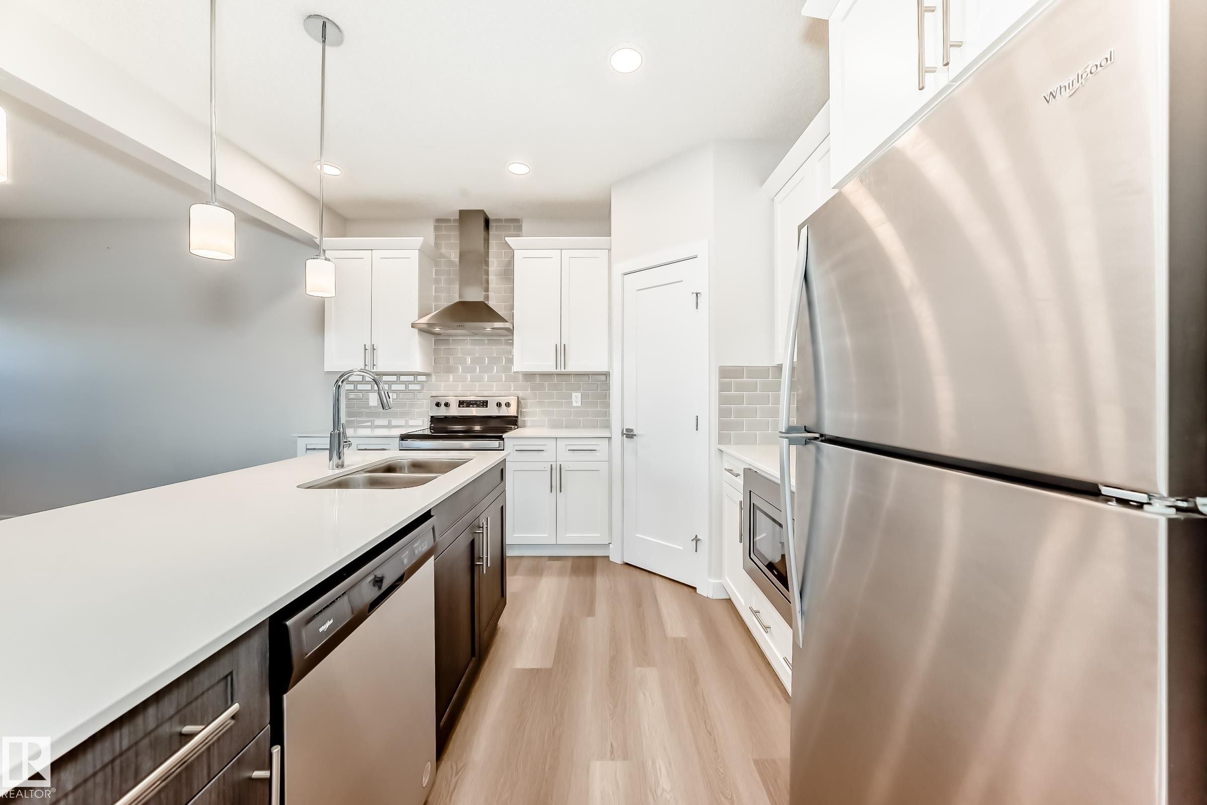 Kitchen featuring stainless steel appliances, two tone cabinetry, decorative light fixtures, light wood-style flooring, and tasteful backsplash - 17926 62A Street, Edmonton, AB - Indoor Photo Showing Kitchen With Double Sink With Upgraded Kitchen