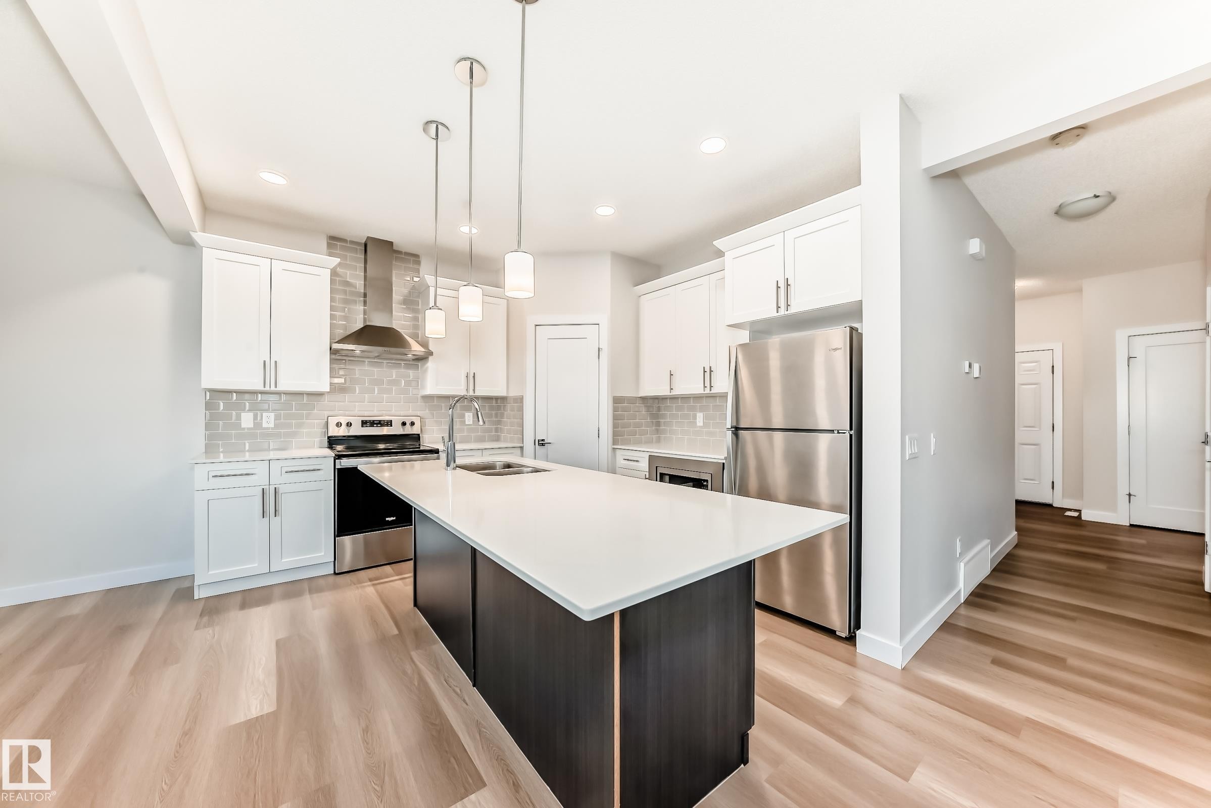 Dual tone kitchen with stainless steel appliances, a kitchen island with sink, dual tone cabinetry, light wood-style floors, and decorative light fixtures - 17926 62A Street, Edmonton, AB - Indoor Photo Showing Kitchen With Double Sink With Upgraded Kitchen