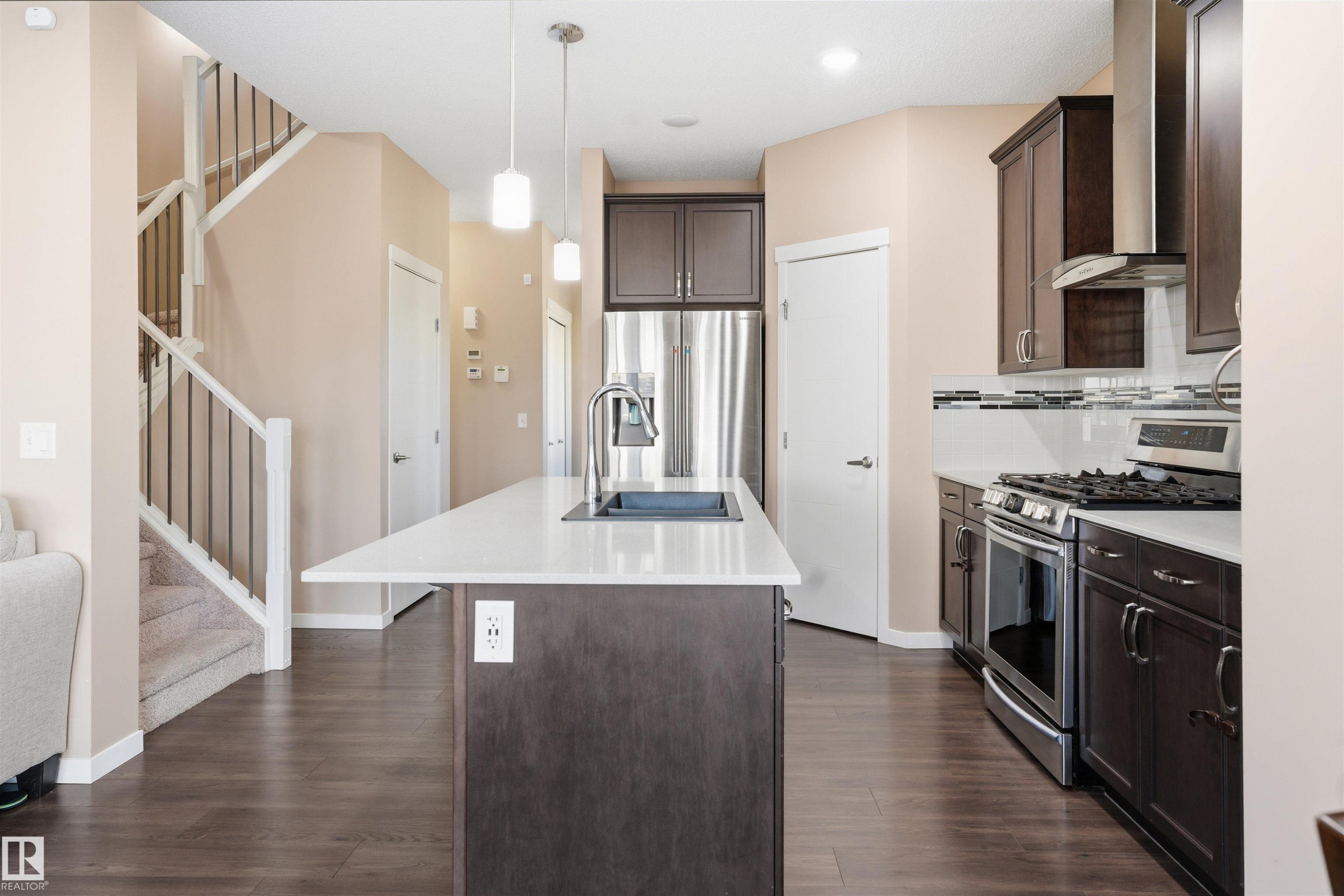 Kitchen with dark wood finish cabinetry, stainless steel appliances, an island with sink, hanging light fixtures, and backsplash - 5003 Andison Close, Edmonton, AB - Indoor Photo Showing Kitchen With Upgraded Kitchen