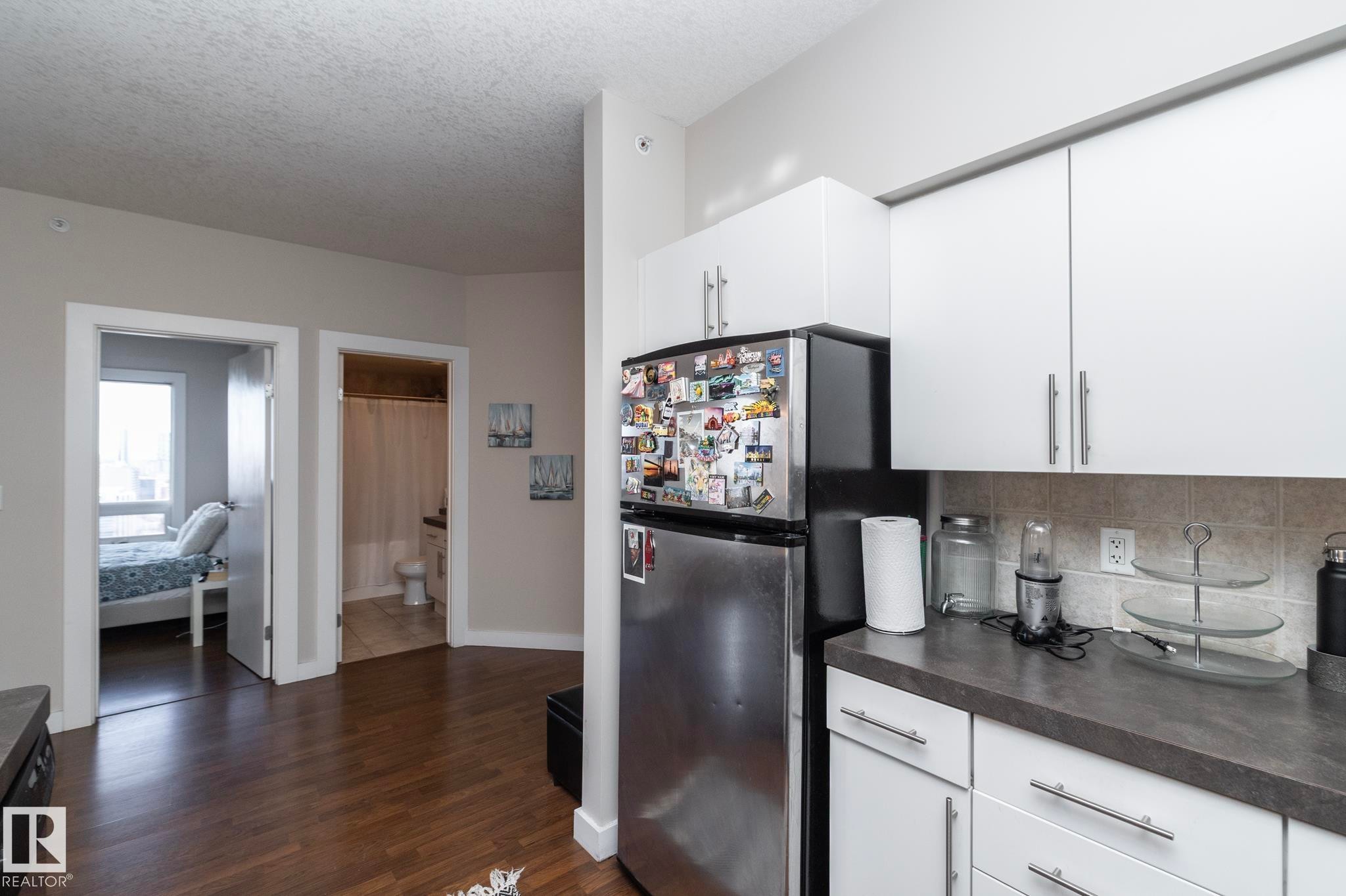 Kitchen with dark countertops, white cabinetry, freestanding refrigerator, a textured ceiling, and dark wood-type flooring - 2005 10136 104 Street, Edmonton, AB - Indoor Photo Showing Kitchen