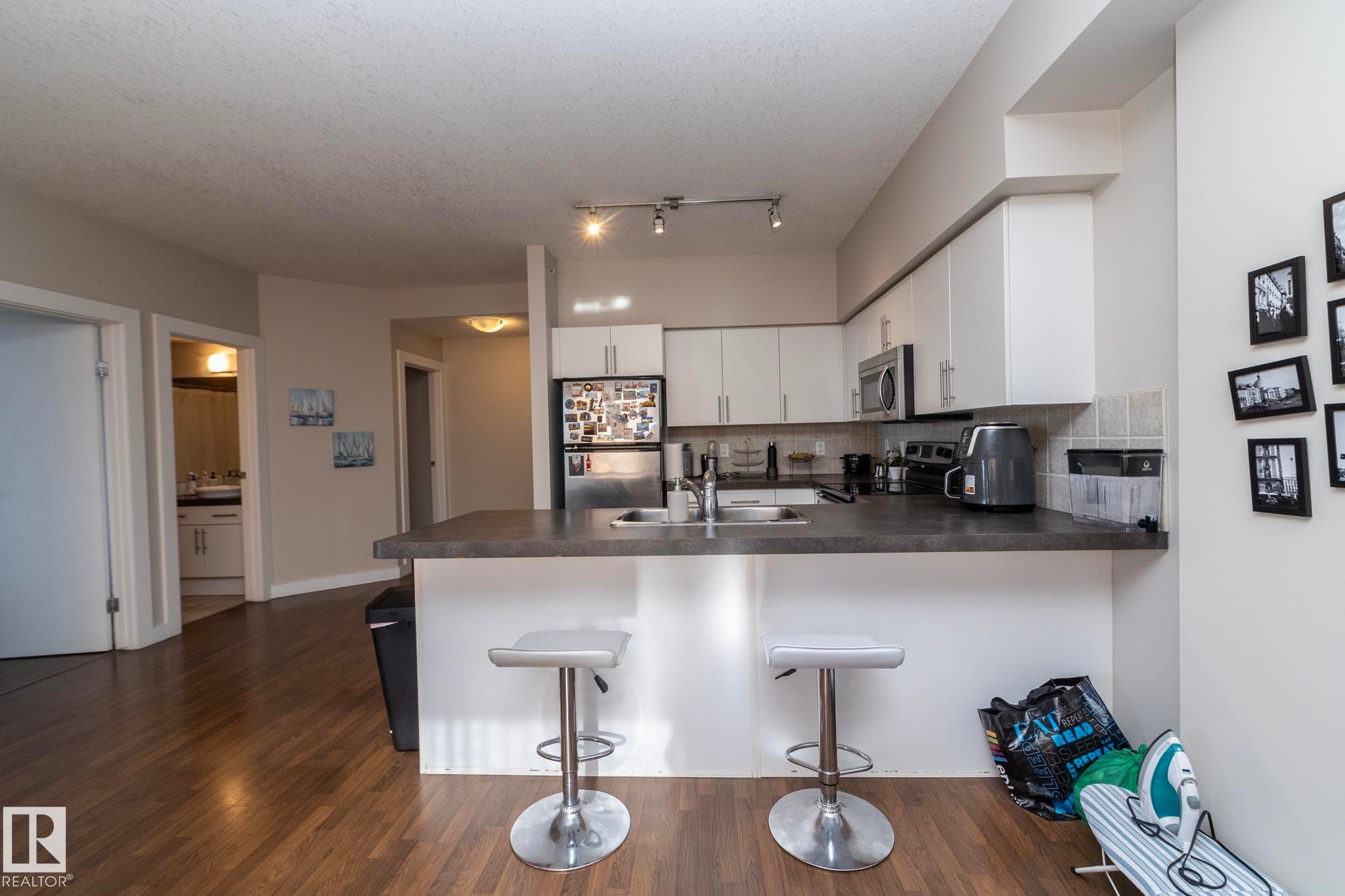 Kitchen featuring a peninsula, stainless steel appliances, white cabinetry, a kitchen breakfast bar, and backsplash - 2005 10136 104 Street, Edmonton, AB - Indoor Photo Showing Kitchen