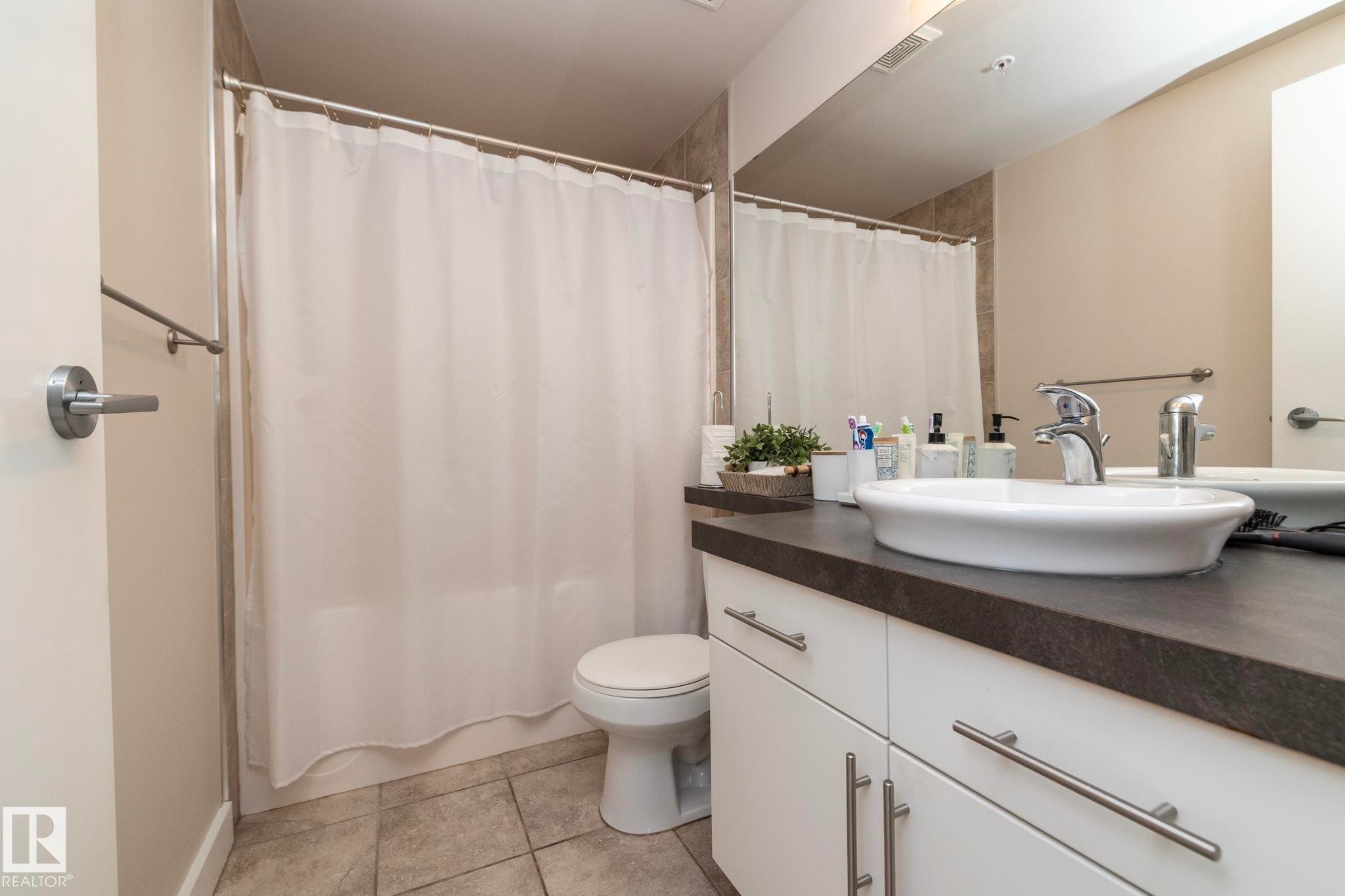 Full bathroom featuring vanity, shower / bath combo with shower curtain, and light tile patterned floors - 2005 10136 104 Street, Edmonton, AB - Indoor Photo Showing Bathroom