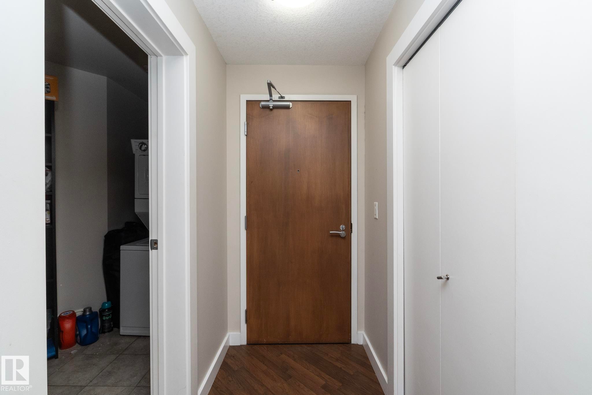 Corridor featuring a textured ceiling, stacked washer and dryer, and dark wood-style floors - 2005 10136 104 Street, Edmonton, AB - Indoor Photo Showing Other Room