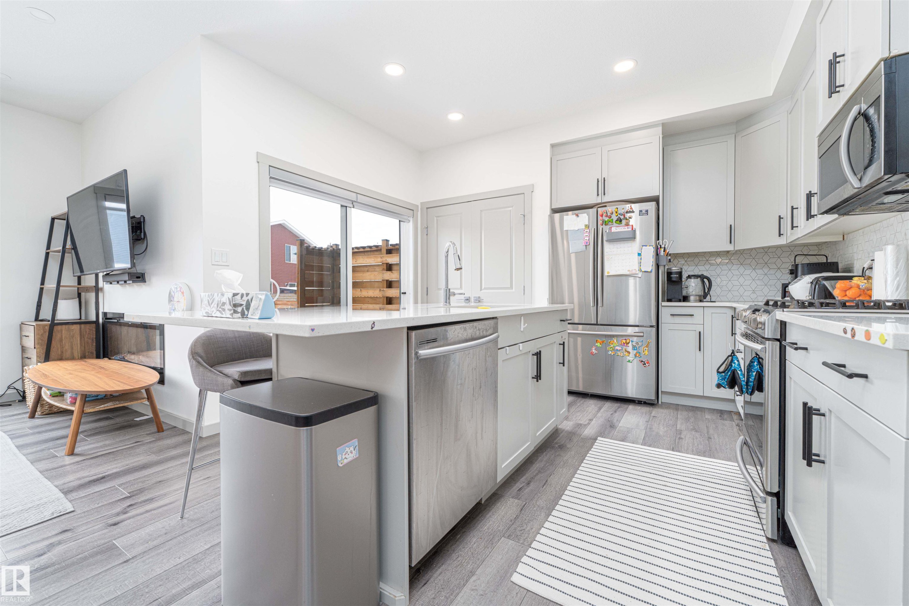Kitchen featuring stainless steel appliances, light stone countertops, light wood-style flooring, a kitchen bar, and decorative backsplash - 2330 Kelly Circle, Edmonton, AB - Indoor Photo Showing Kitchen