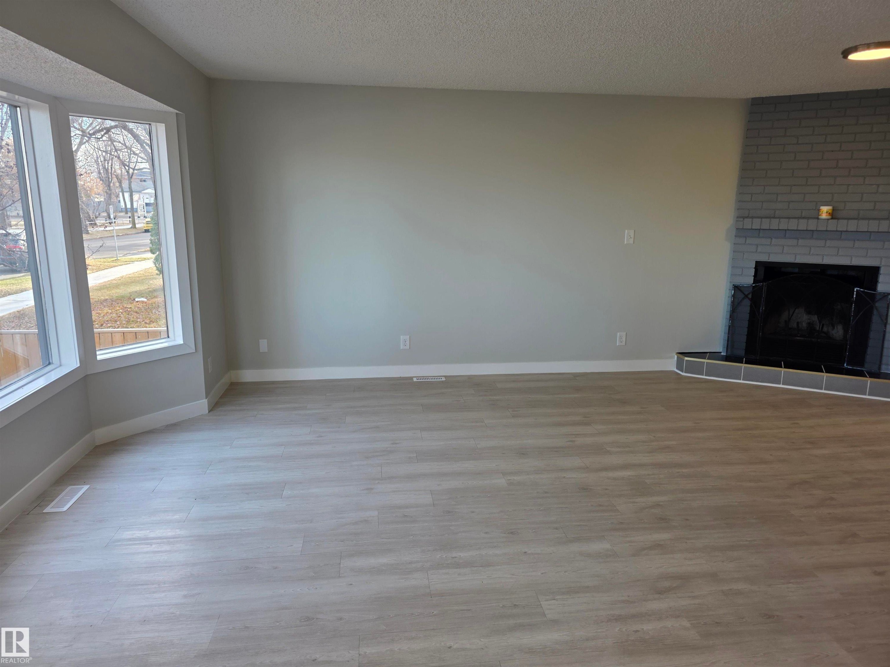 Unfurnished living room with a fireplace, a textured ceiling, and light wood-style flooring - Edmonton, AB - Indoor With Fireplace