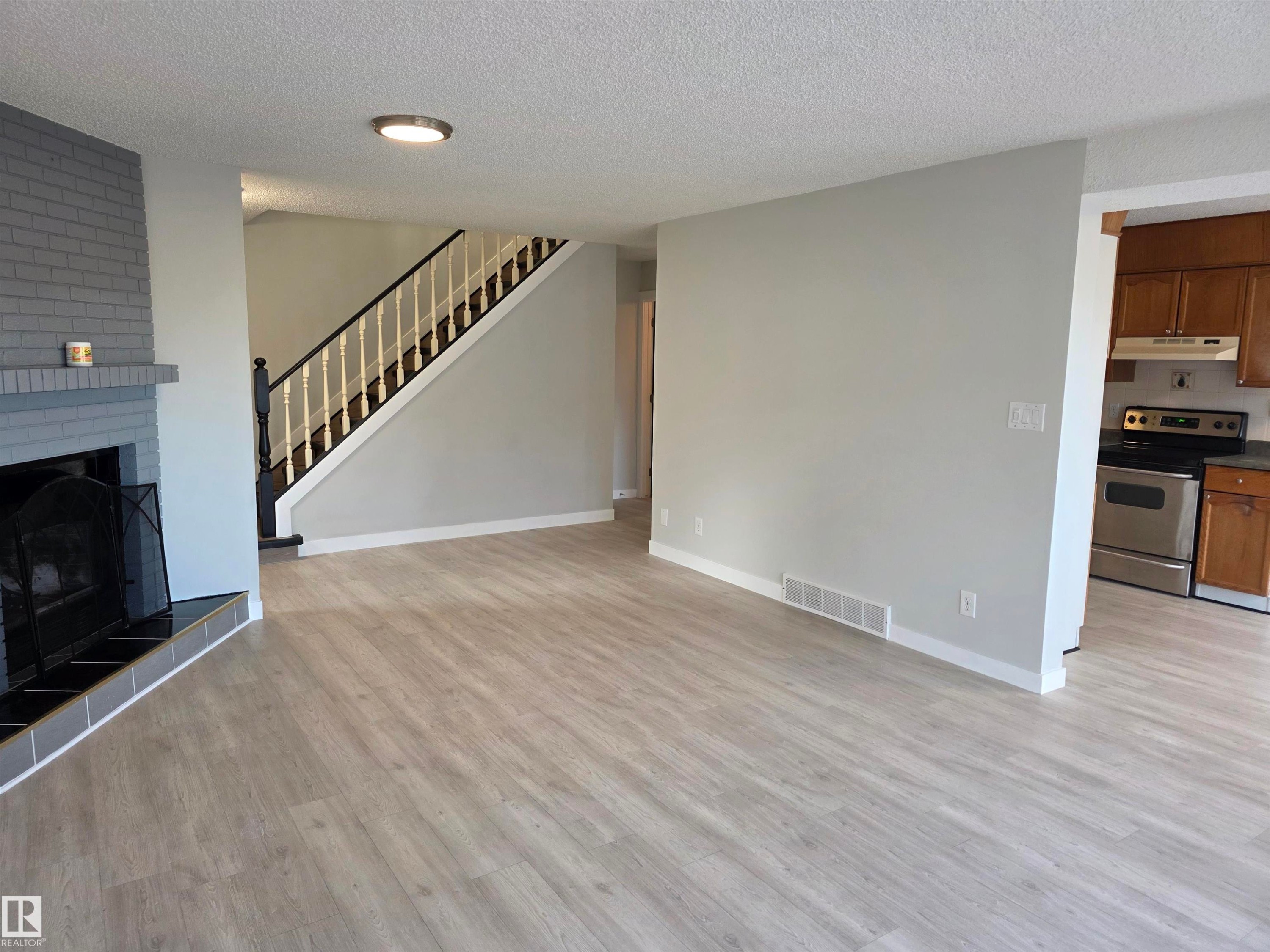 Unfurnished living room featuring a large fireplace, light wood finished floors, and a textured ceiling - Edmonton, AB - Indoor Photo Showing Living Room With Fireplace