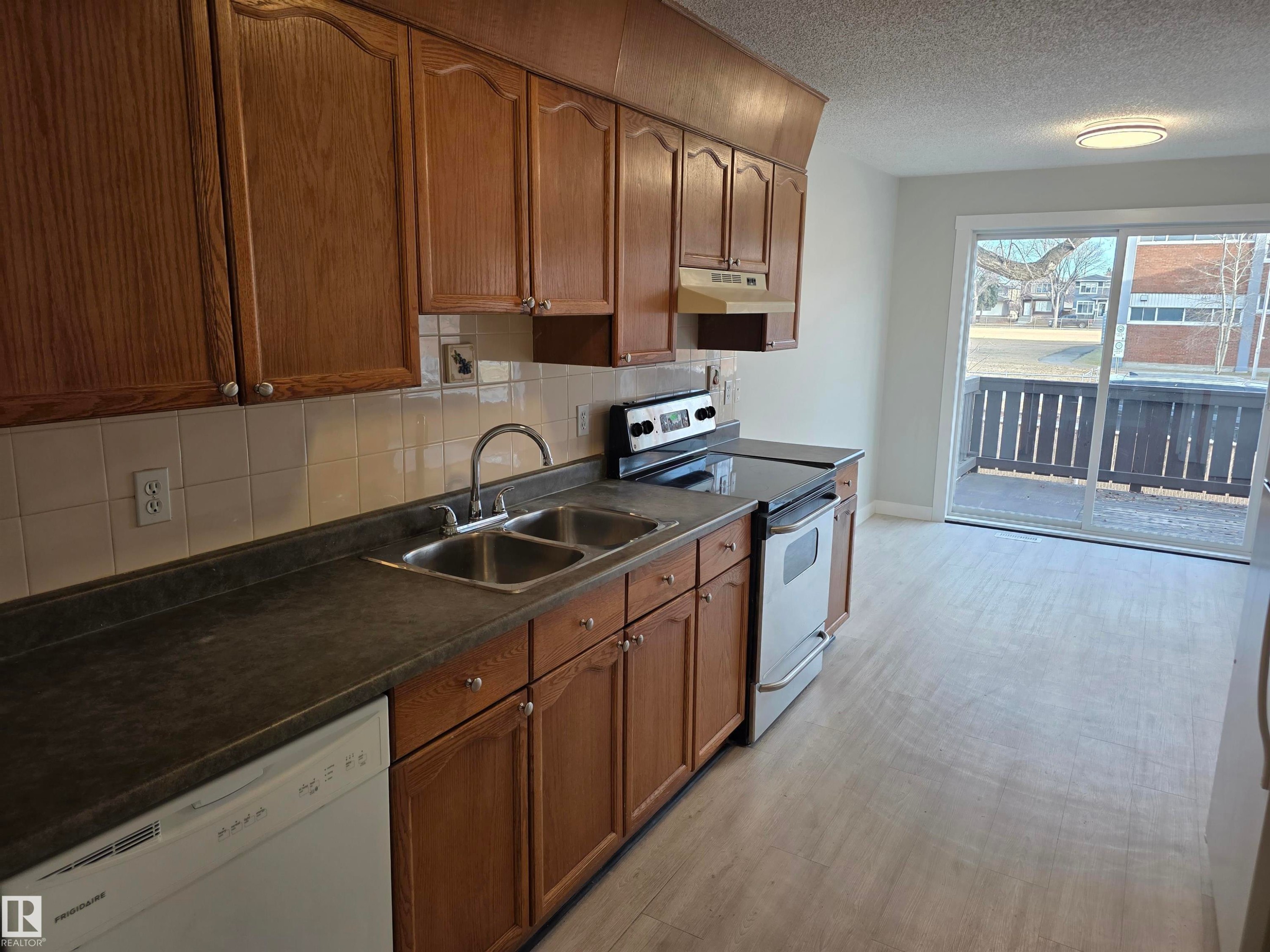 Kitchen with stainless steel electric stove, dishwasher, backsplash, dark countertops, and a textured ceiling - Edmonton, AB - Indoor Photo Showing Kitchen With Double Sink