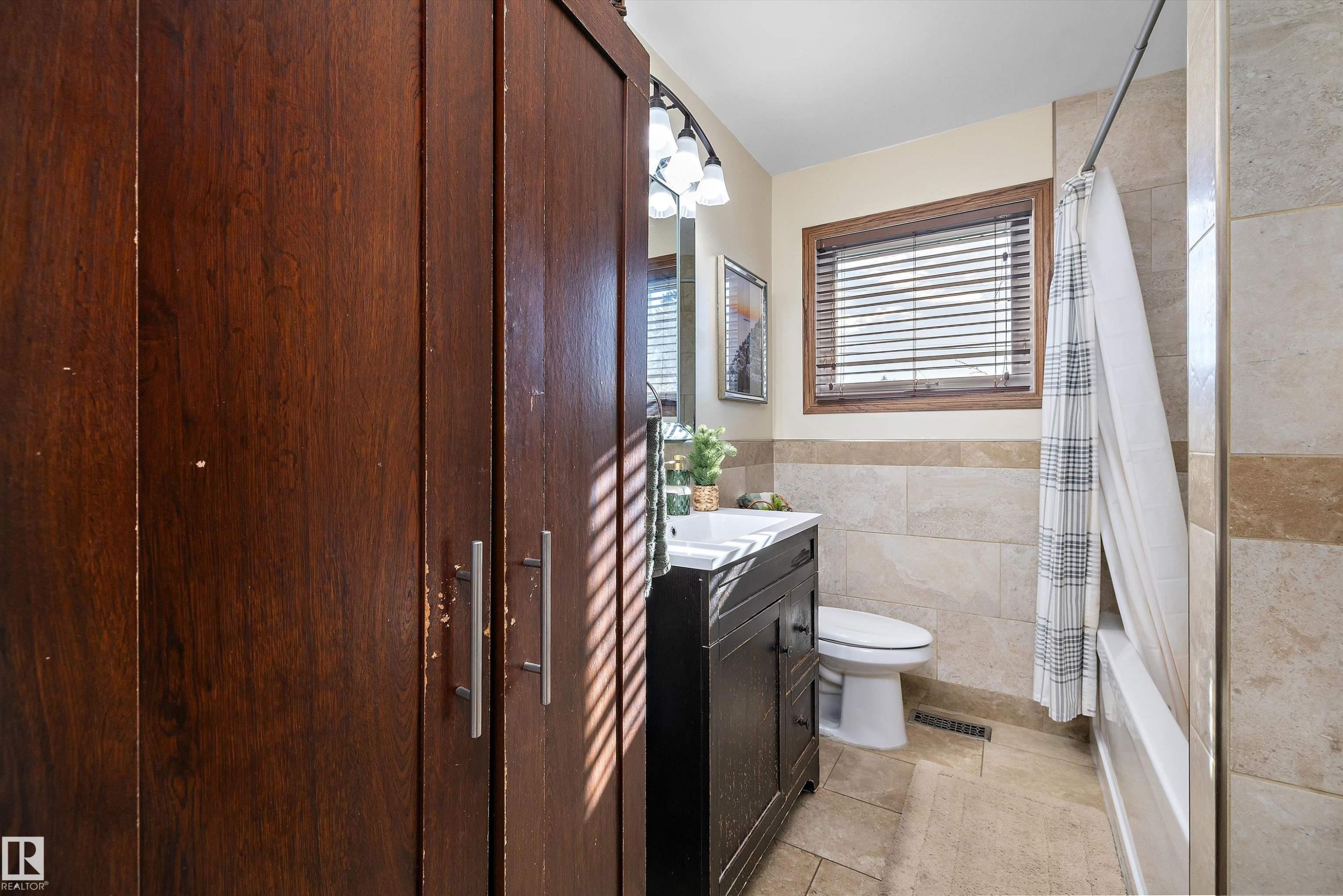 Full bath featuring vanity, shower / bathtub combination with curtain, tile walls, light tile patterned floors, and wainscoting - 5703 143 Avenue, Edmonton, AB - Indoor Photo Showing Bathroom