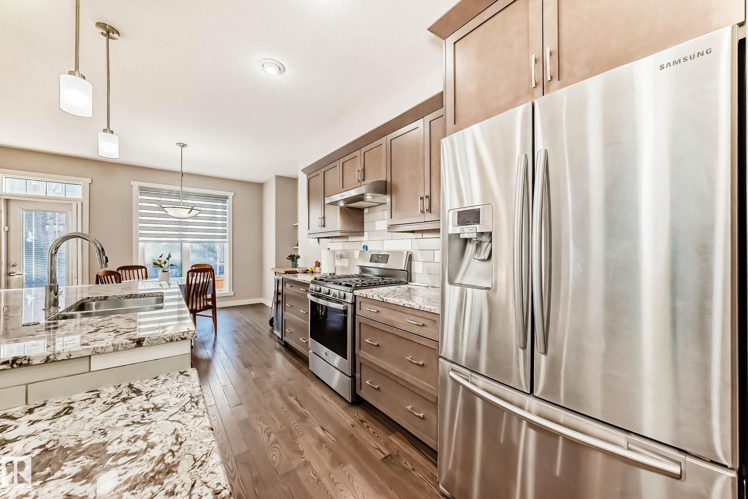 Kitchen with stainless steel appliances, dark wood-type flooring, hanging light fixtures, light stone counters, and wood finish cabinets - 7719 Getty Wynd, Edmonton, AB - Indoor Photo Showing Kitchen With Upgraded Kitchen