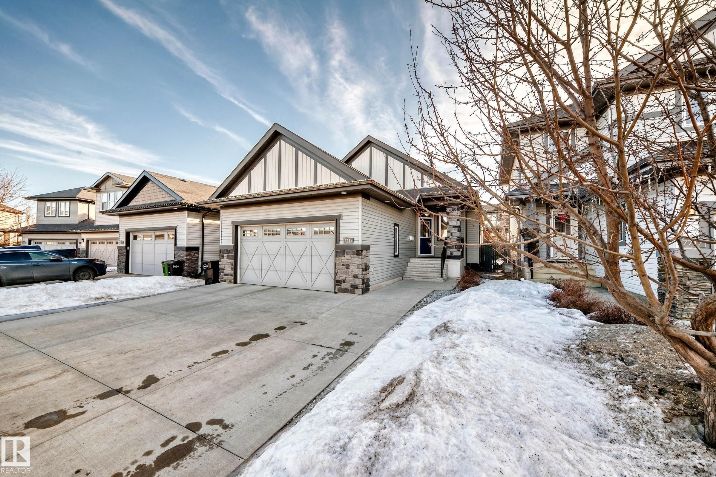 View of front facade featuring board and batten siding, concrete driveway, stone siding, and a garage - 7719 Getty Wynd, Edmonton, AB - Outdoor With Facade