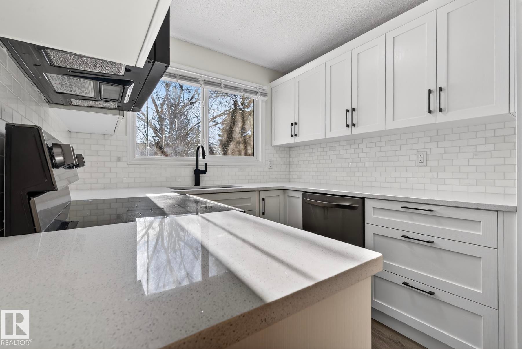 Kitchen with white cabinetry, light stone counters, ventilation hood, dishwasher, and a textured ceiling - 9969 171 Ave, Edmonton, AB - Indoor Photo Showing Other Room