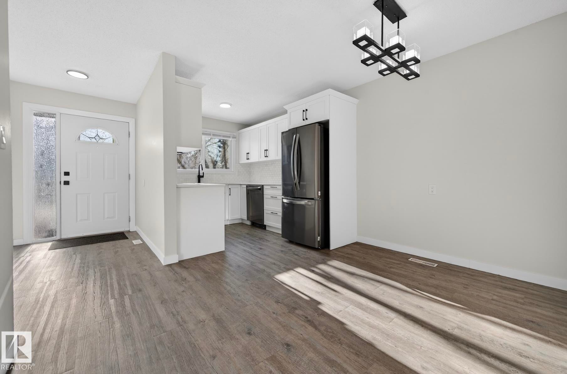 Kitchen with white cabinetry, light countertops, stainless steel appliances, dark wood-style flooring, and a chandelier - 9969 171 Ave, Edmonton, AB - Indoor Photo Showing Kitchen