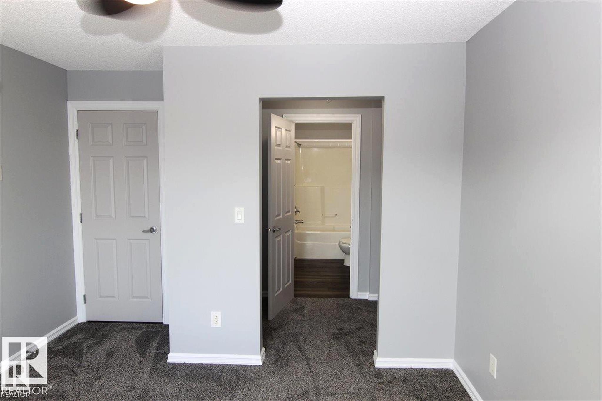 Unfurnished bedroom with dark carpet, ensuite bathroom, a textured ceiling, and ceiling fan - 404 4407 23 Street, Edmonton, AB - Indoor Photo Showing Other Room
