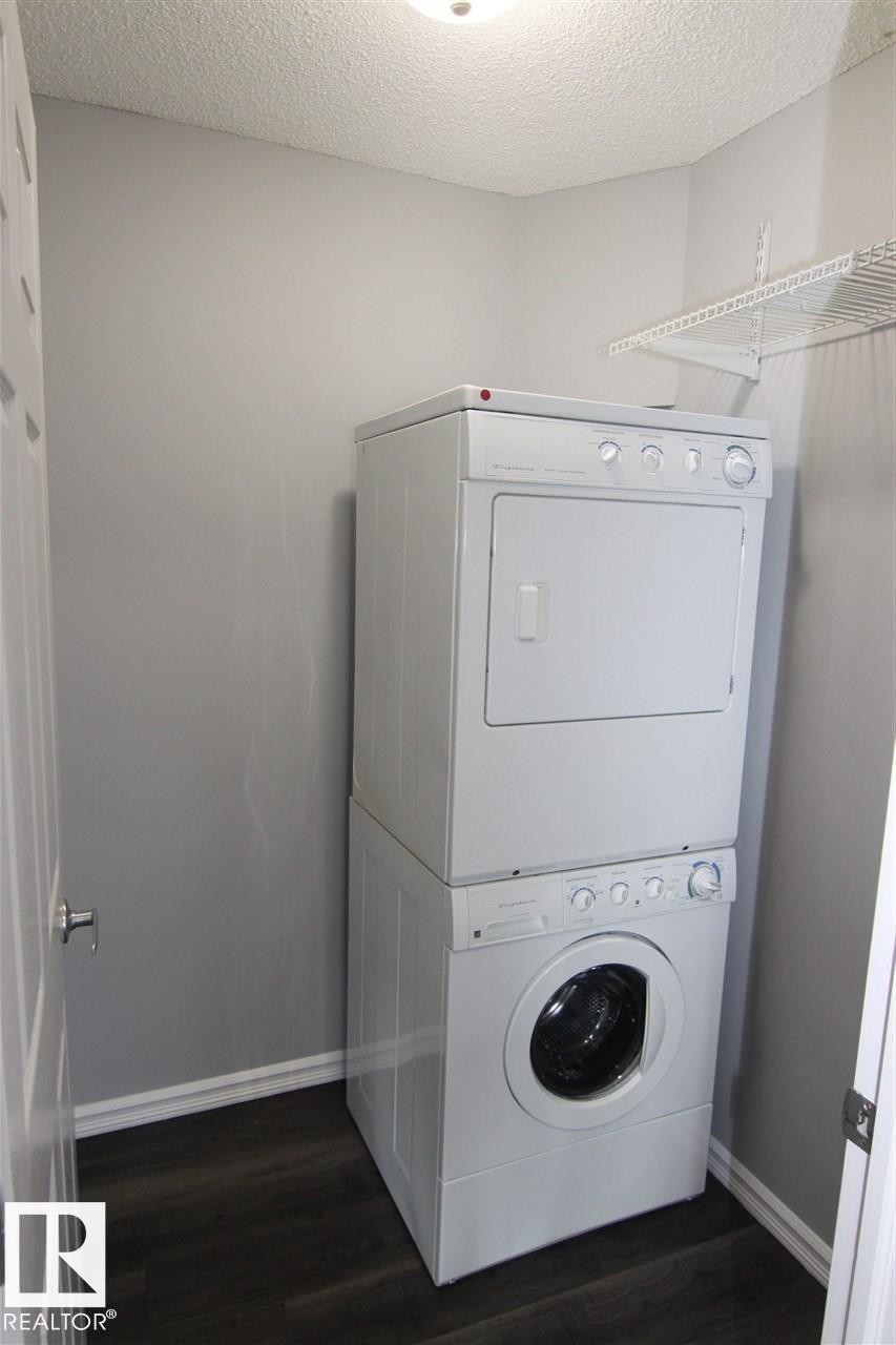 Laundry room featuring stacked washer and clothes dryer, dark wood finished floors, and a textured ceiling - 404 4407 23 Street, Edmonton, AB - Indoor Photo Showing Laundry Room