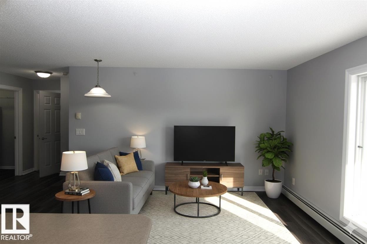 Living room with a baseboard heating unit, wood finished floors, and a textured ceiling - 404 4407 23 Street, Edmonton, AB - Indoor Photo Showing Living Room