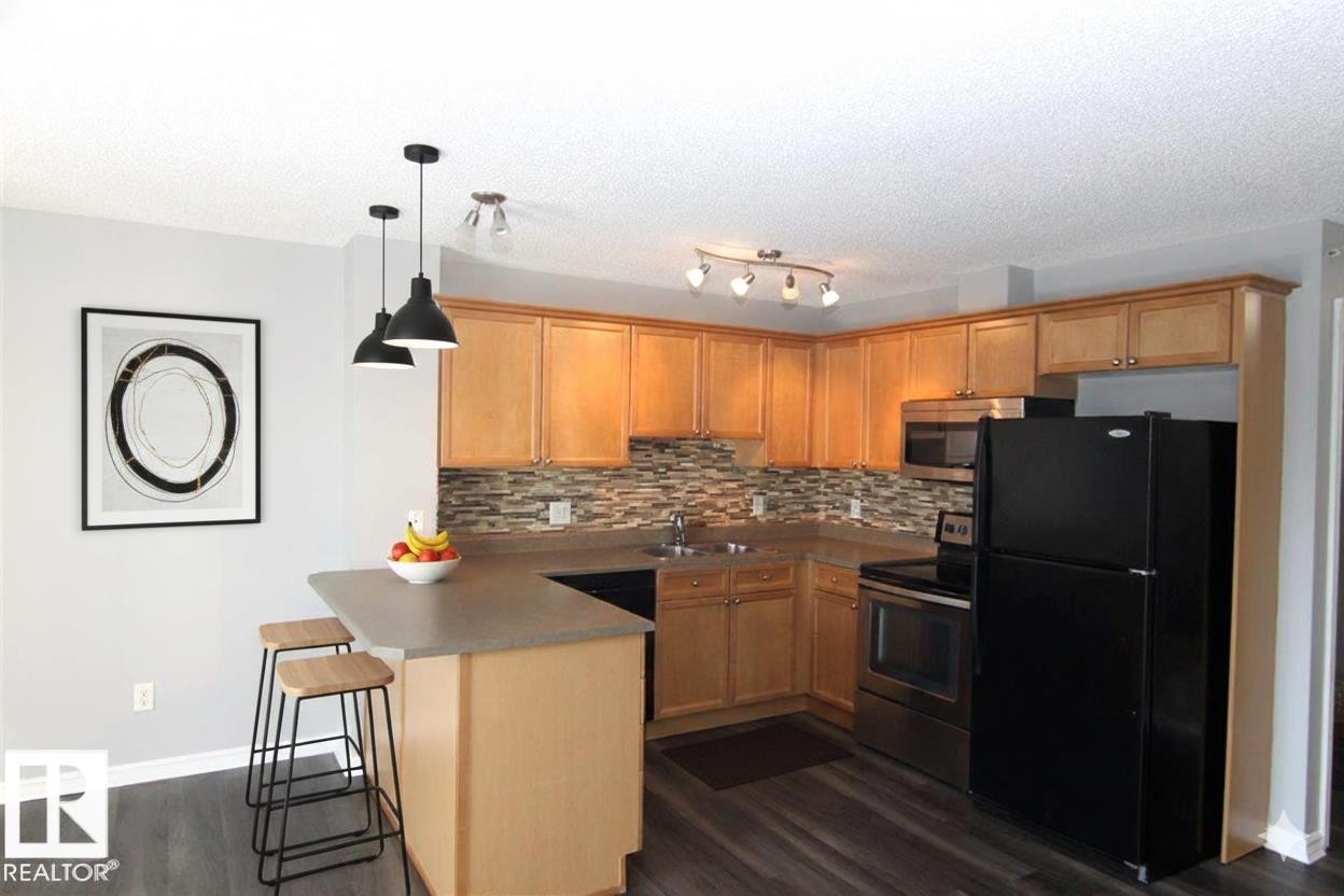 Kitchen with stainless steel appliances, a peninsula, a breakfast bar, dark wood-type flooring, and hanging light fixtures - 404 4407 23 Street, Edmonton, AB - Indoor Photo Showing Kitchen