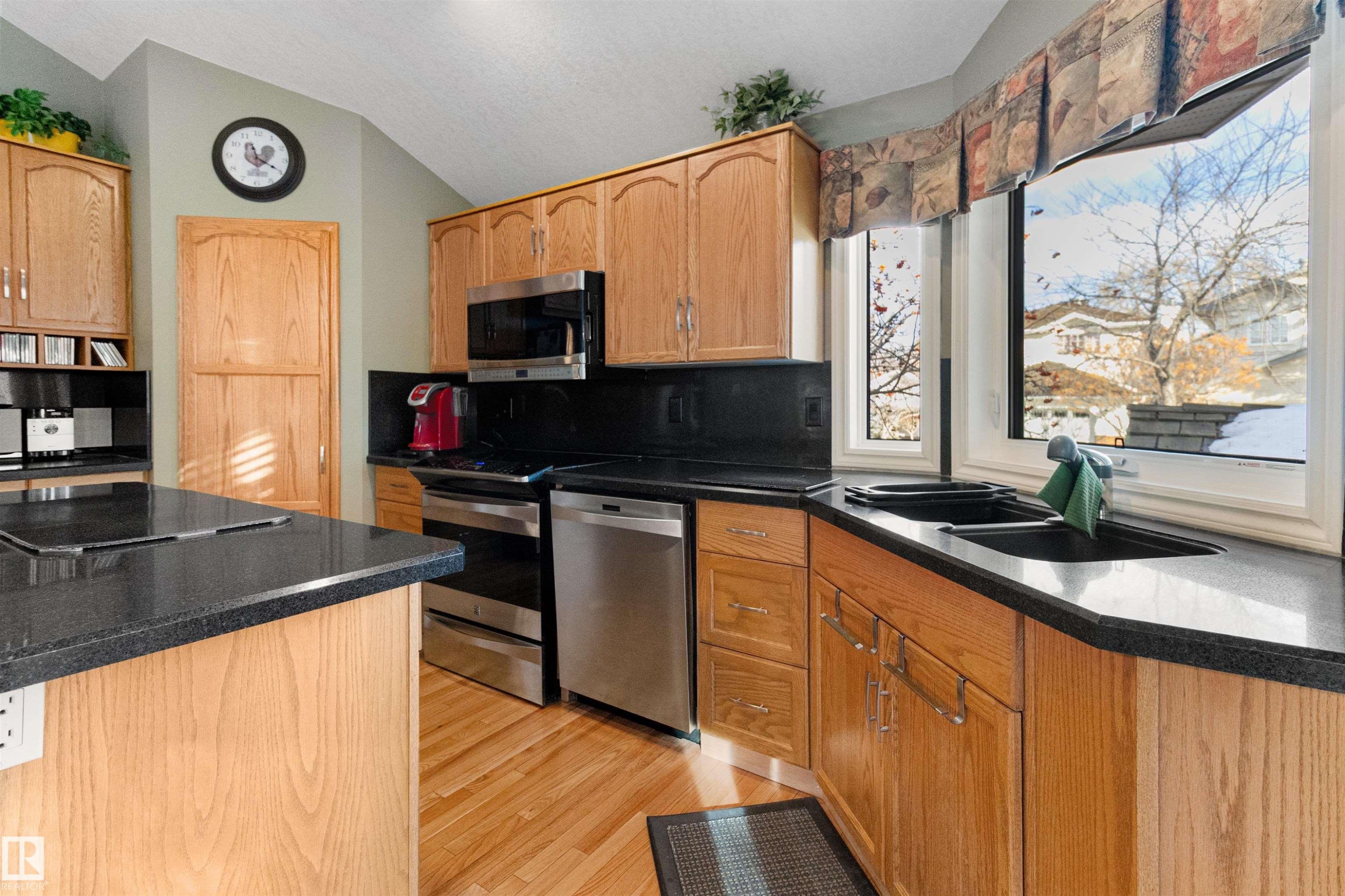 Kitchen with stainless steel appliances, light wood-style flooring, decorative backsplash, vaulted ceiling, and dark stone counters - 519 Buchanan Road, Edmonton, AB - Indoor Photo Showing Kitchen With Double Sink