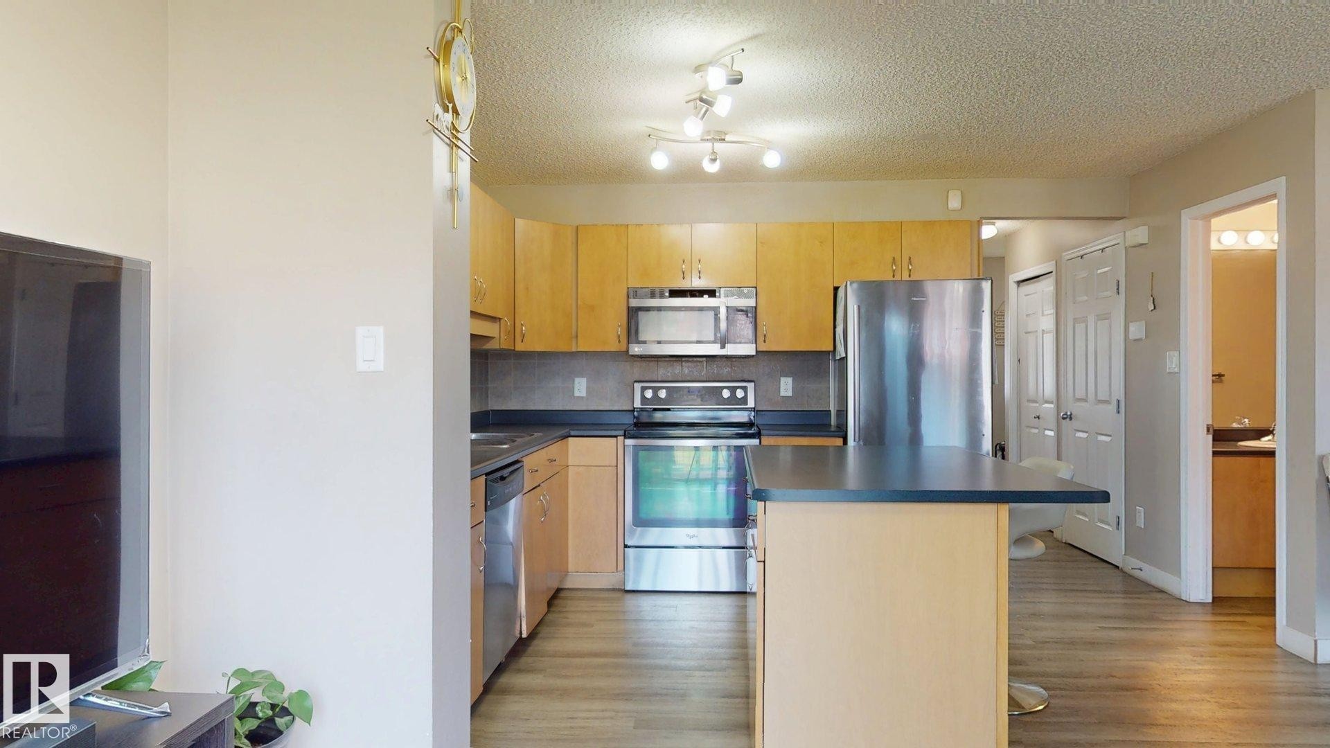 Kitchen featuring stainless steel appliances, a kitchen island, tasteful backsplash, dark countertops, and a breakfast bar - 1150 37B Avenue, Edmonton, AB - Indoor Photo Showing Kitchen With Stainless Steel Kitchen