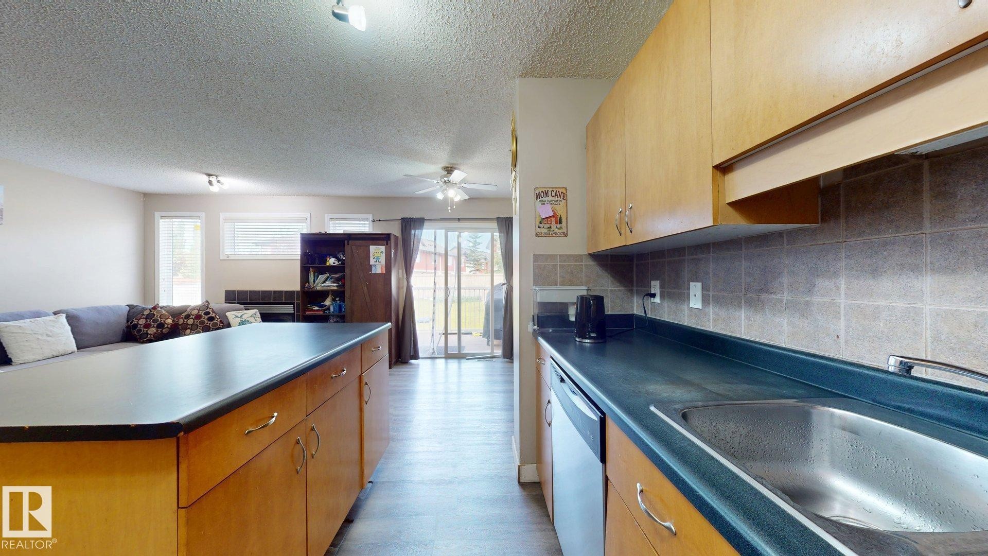Kitchen featuring open floor plan, dark countertops, a textured ceiling, dishwasher, and decorative backsplash - 1150 37B Avenue, Edmonton, AB - Indoor Photo Showing Kitchen