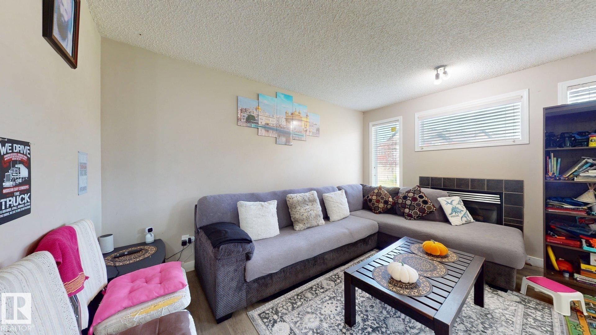 Living area featuring a tile fireplace, a textured ceiling, and wood finished floors - 1150 37B Avenue, Edmonton, AB - Indoor Photo Showing Living Room