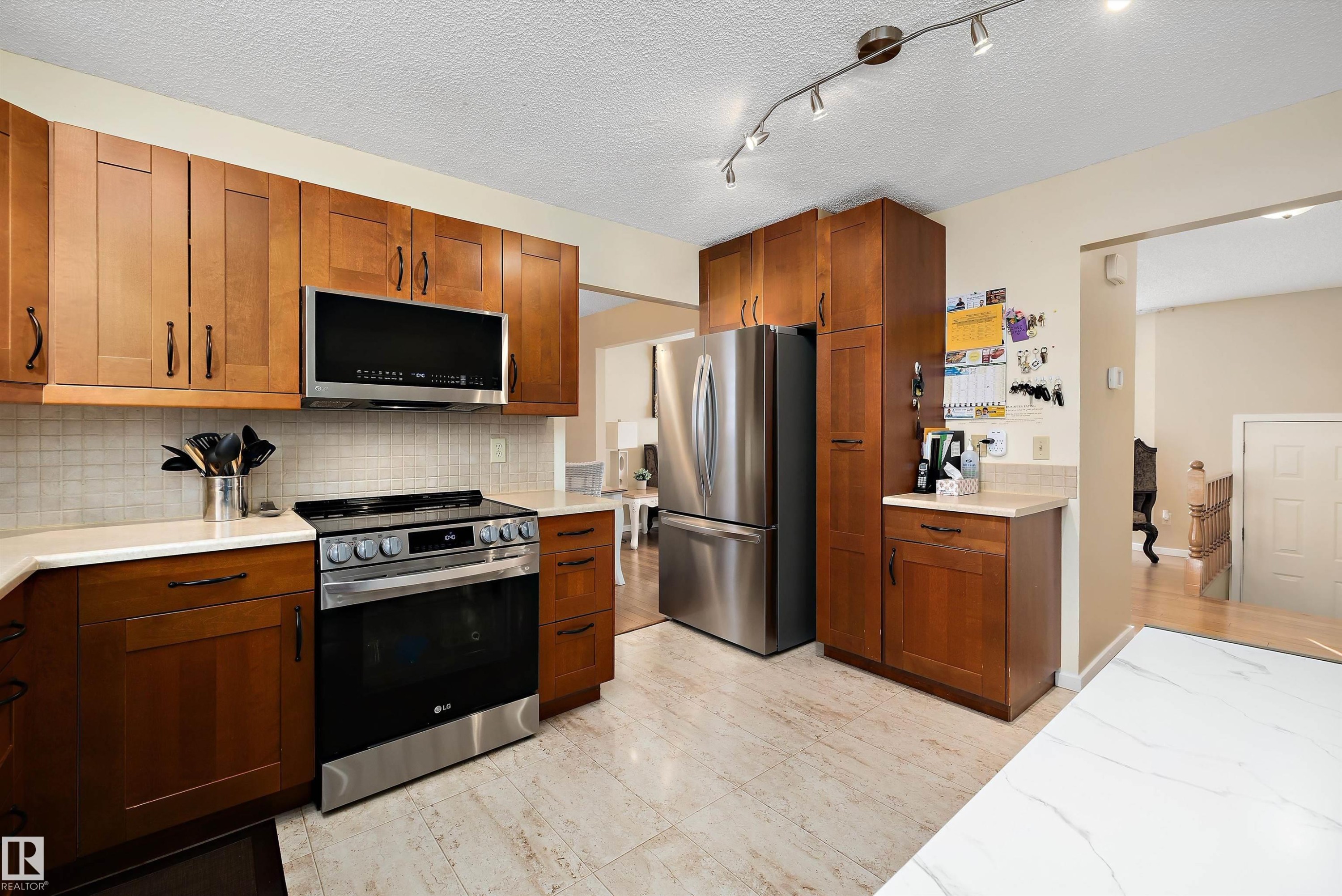 Kitchen featuring stainless steel appliances, wood finish cabinets, tasteful backsplash, a textured ceiling, and rail lighting - 9804 156 Avenue, Edmonton, AB - Indoor Photo Showing Kitchen With Stainless Steel Kitchen