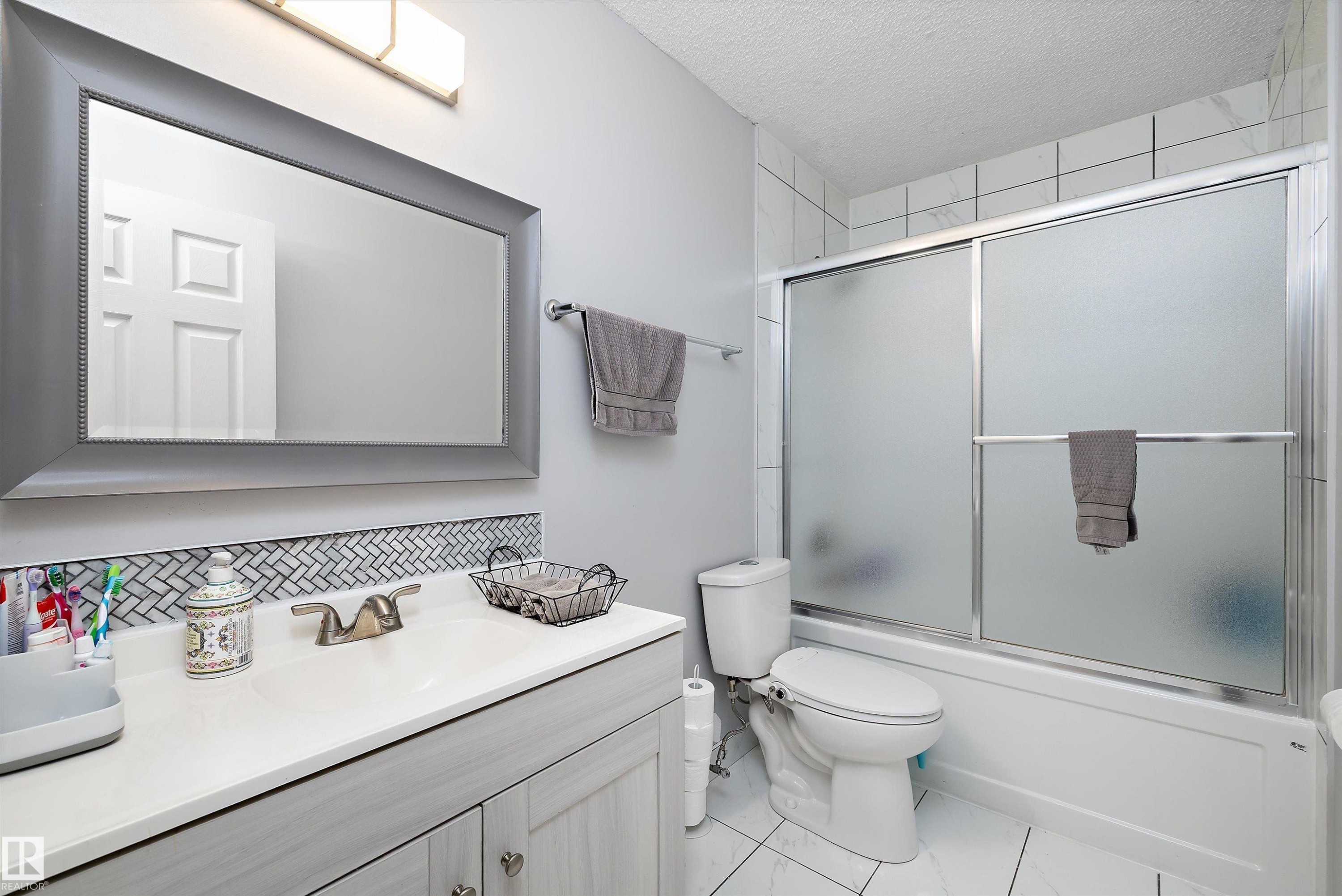 Full bathroom with vanity, enclosed tub / shower combo, a textured ceiling, and tasteful backsplash - 9804 156 Avenue, Edmonton, AB - Indoor Photo Showing Bathroom