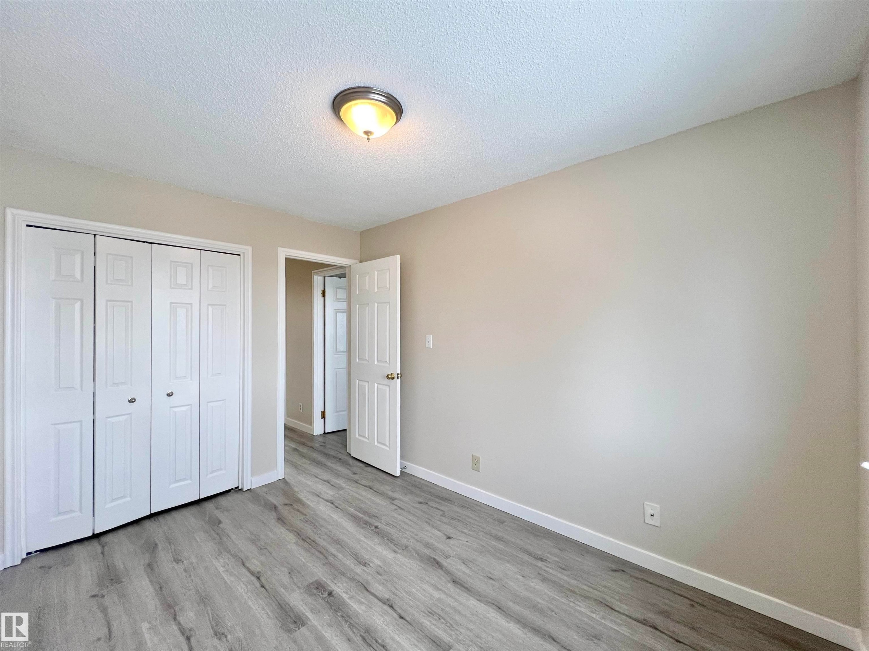 Unfurnished bedroom featuring a textured ceiling, a closet, and light wood-style floors - 11357 22 Avenue, Edmonton, AB - Indoor Photo Showing Other Room