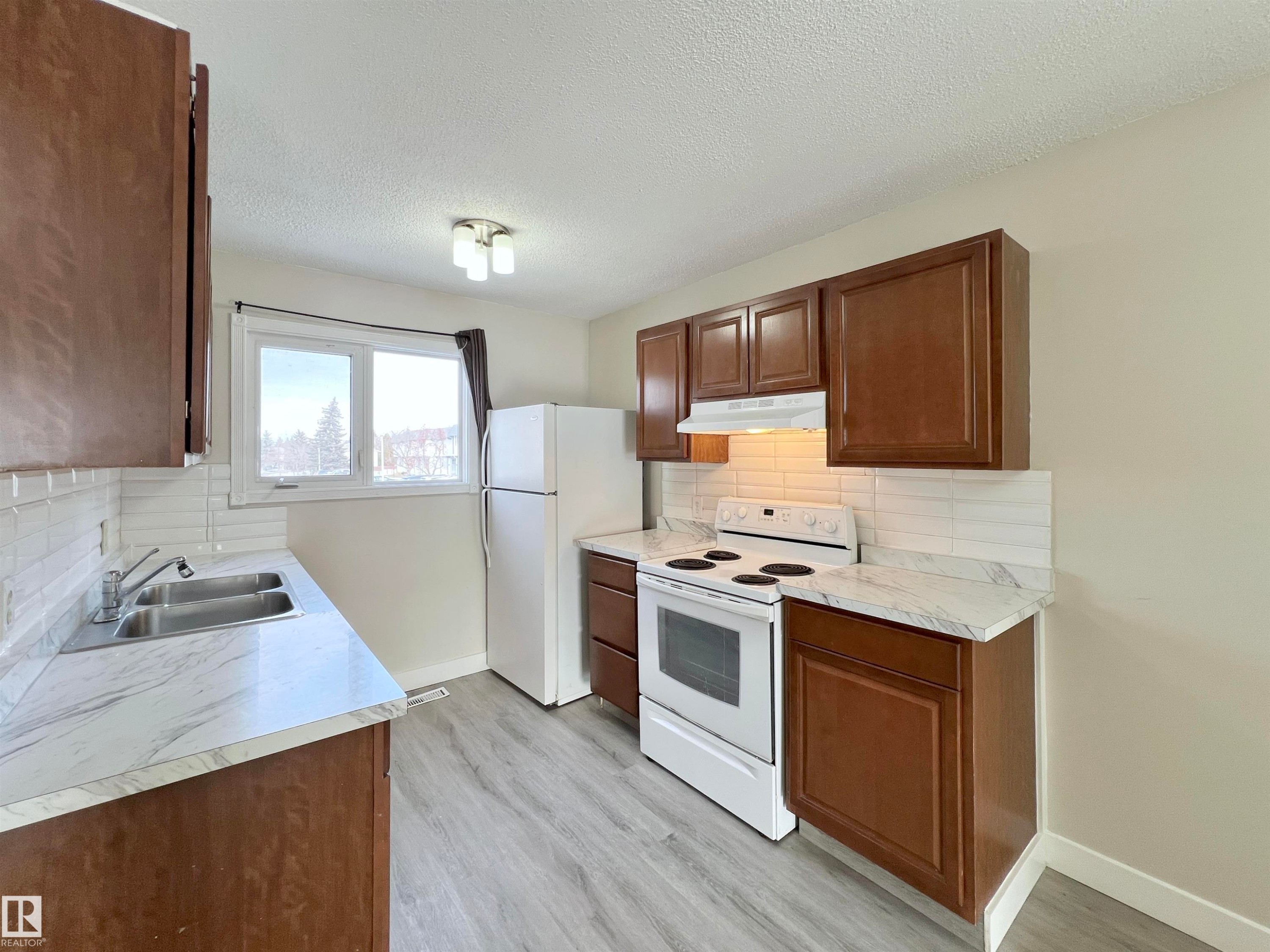 Kitchen with white appliances, light countertops, decorative backsplash, light wood-style floors, and a textured ceiling - 11357 22 Avenue, Edmonton, AB - Indoor Photo Showing Kitchen With Double Sink