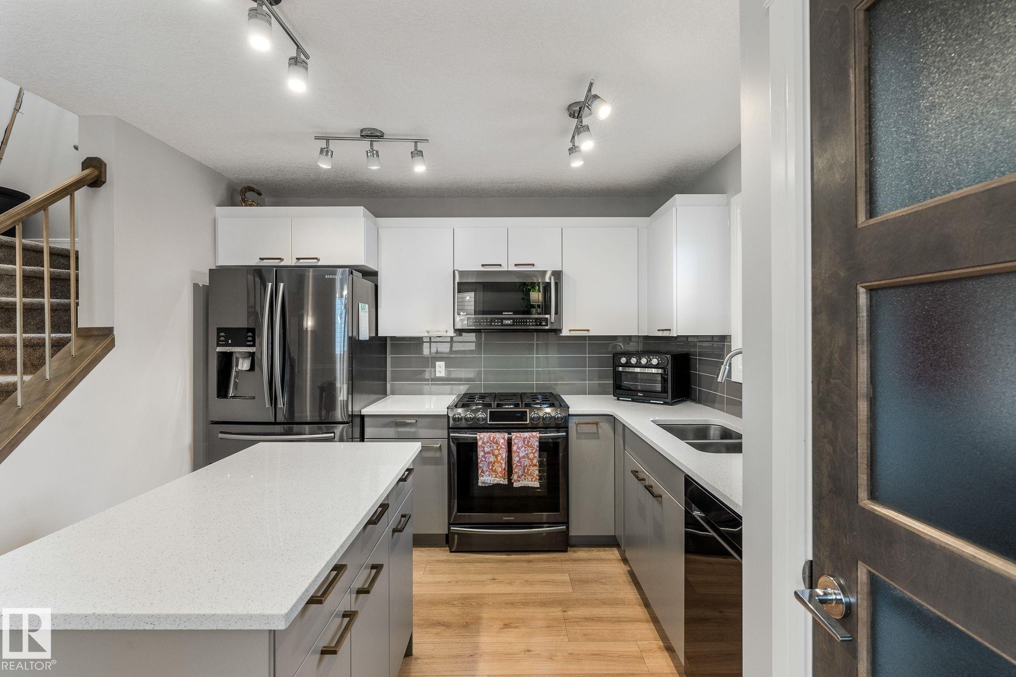 Dual tone kitchen with stainless steel appliances, gas stove, a kitchen island, light wood-type flooring, decorative backsplash, and dual tone cabinetry - 89 Hewitt Circle, Spruce Grove, AB - Indoor Photo Showing Kitchen With Double Sink With Upgraded Kitchen