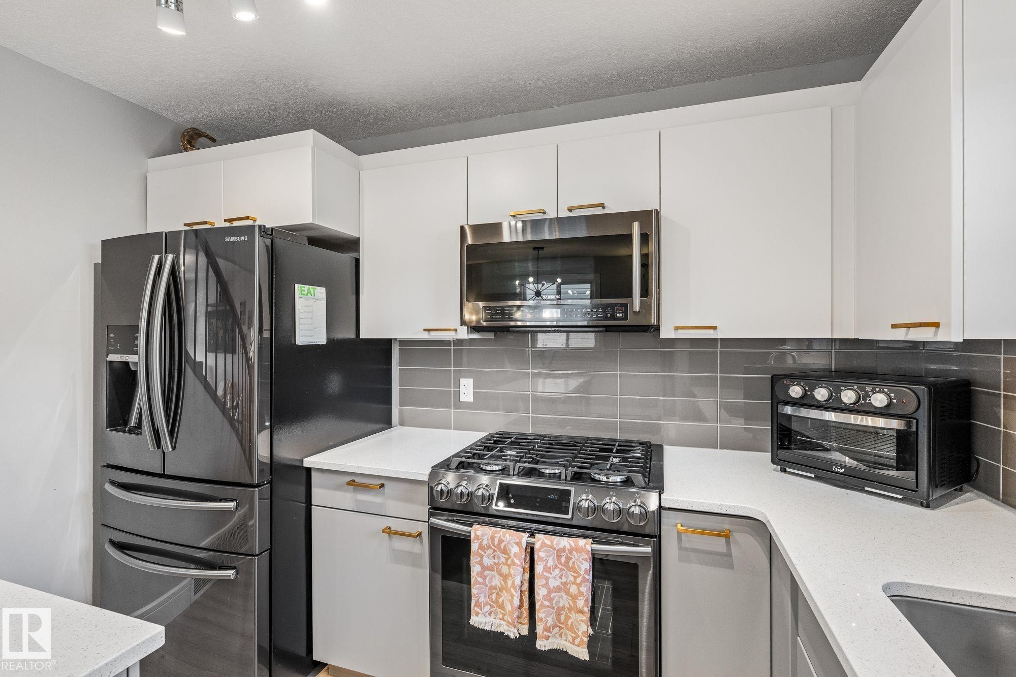 Dual tone kitchen with stainless steel appliances, gas stove, a kitchen island, light wood-type flooring, decorative backsplash, and dual tone cabinetry - 89 Hewitt Circle, Spruce Grove, AB - Indoor Photo Showing Kitchen