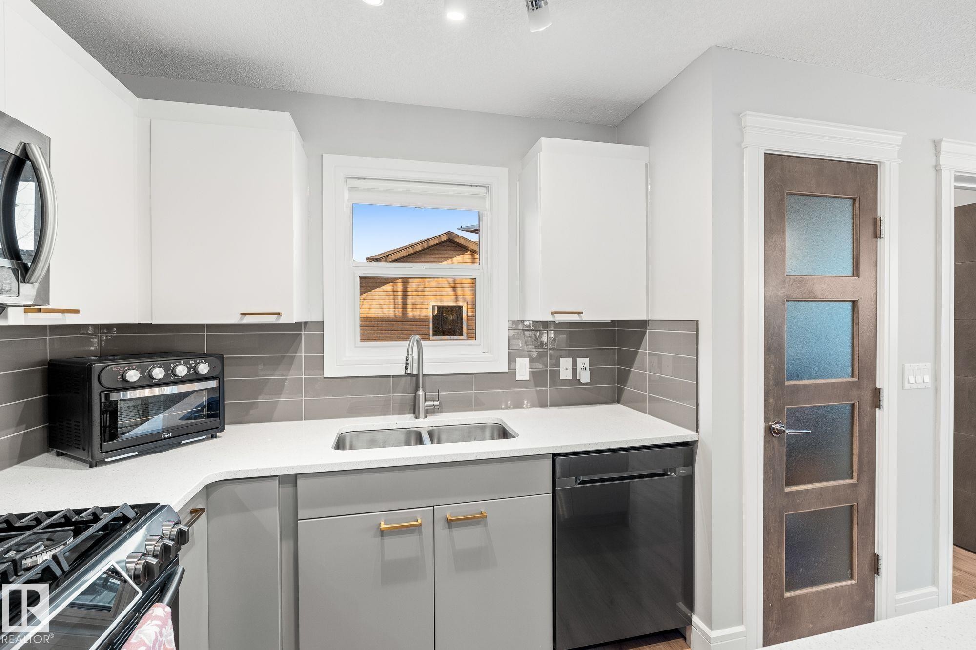 Dual tone kitchen with stainless steel appliances, gas stove, a kitchen island, light wood-type flooring, decorative backsplash, and dual tone cabinetry - 89 Hewitt Circle, Spruce Grove, AB - Indoor Photo Showing Kitchen With Double Sink