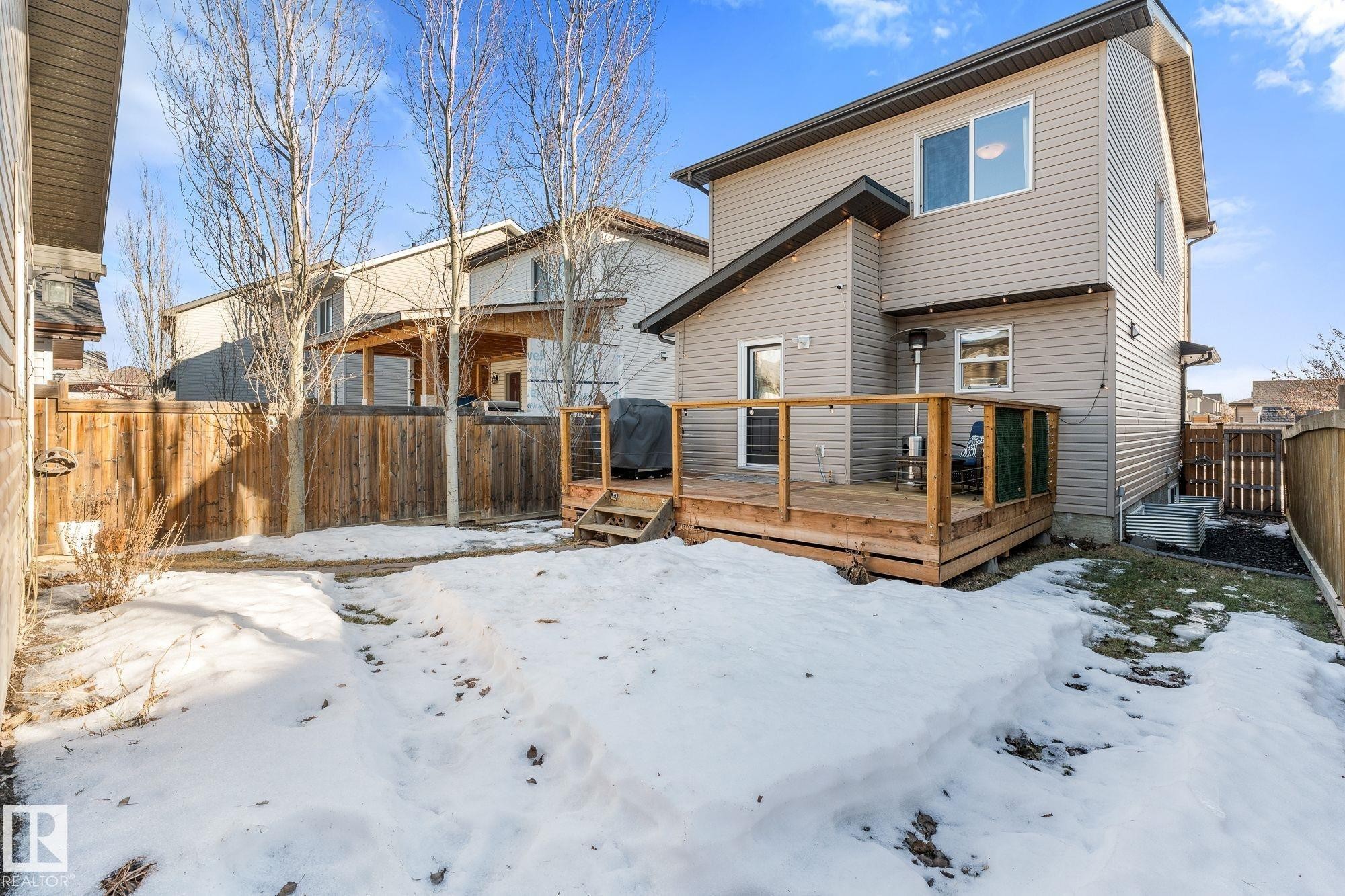 Landscaped backyard featuring a wooden deck, exterior lights, mature trees, and a pathway to the double detached garage - 89 Hewitt Circle, Spruce Grove, AB - Outdoor