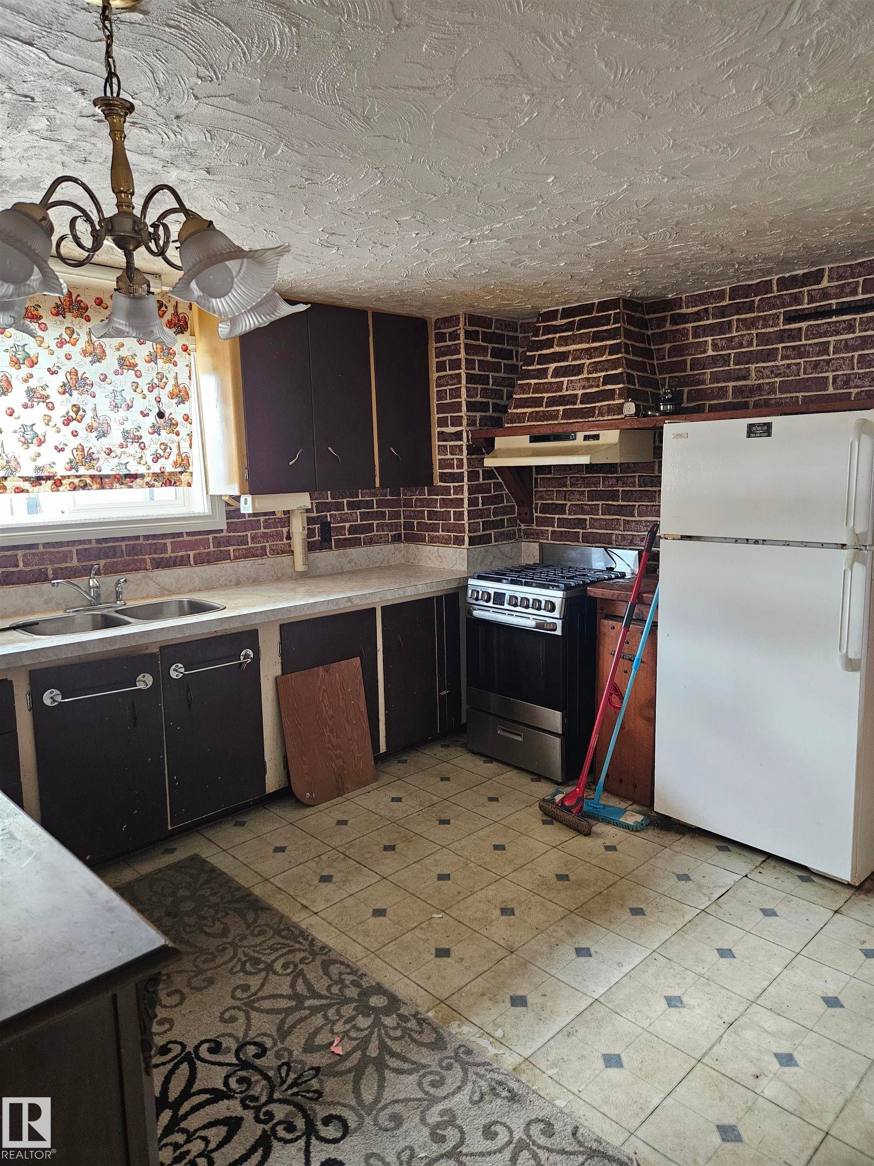 Kitchen with freestanding refrigerator, stainless steel range with gas stovetop, light countertops, open shelves, and a textured ceiling - 5314 57 Street, Cold Lake, AB - Indoor