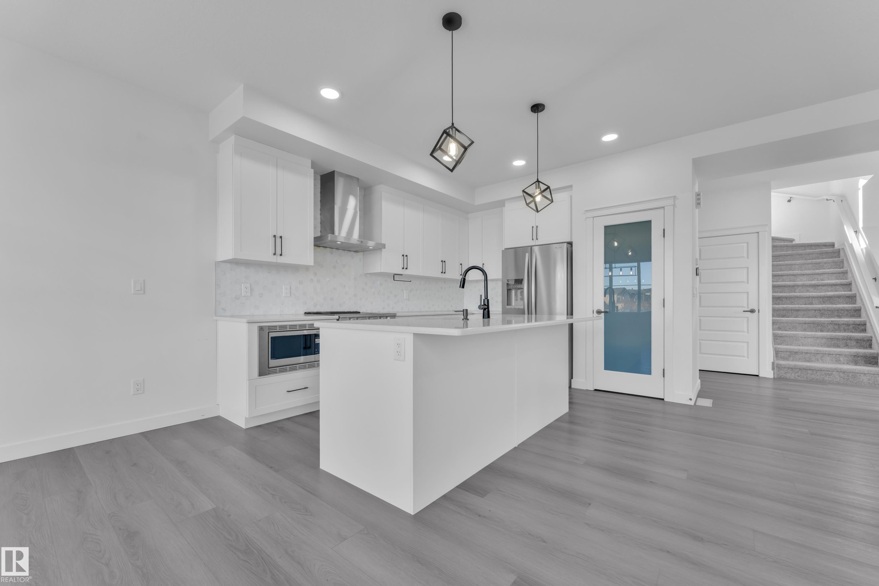 Kitchen with white cabinets, an island with sink, pendant lighting, backsplash, and light wood-style floors - 1822 Collip View, Edmonton, AB