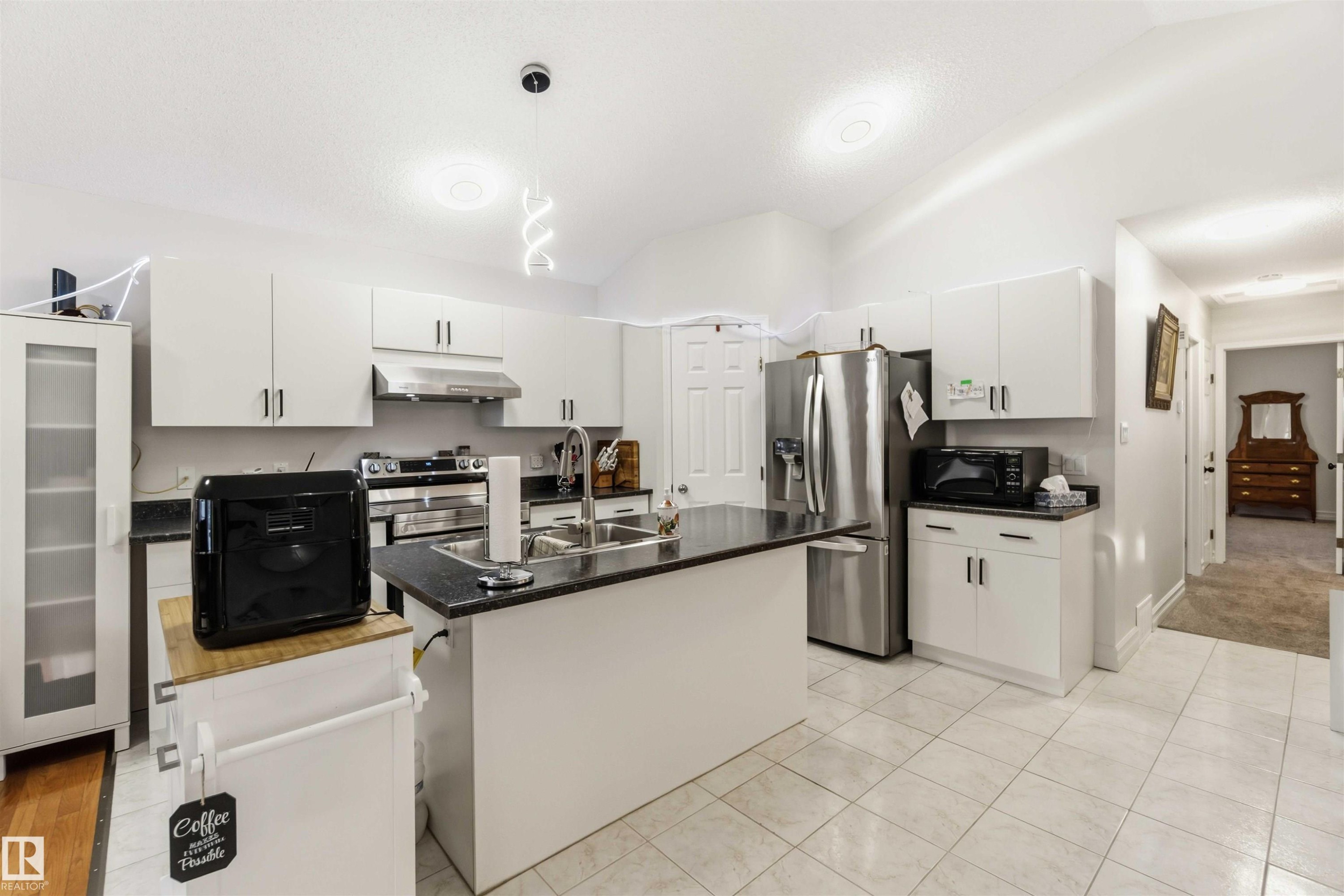 Kitchen with white cabinets, pendant lighting, lofted ceiling, a kitchen island with sink, and stainless steel appliances - 1706 Turvey Bend, Edmonton, AB - Indoor Photo Showing Kitchen With Stainless Steel Kitchen With Double Sink