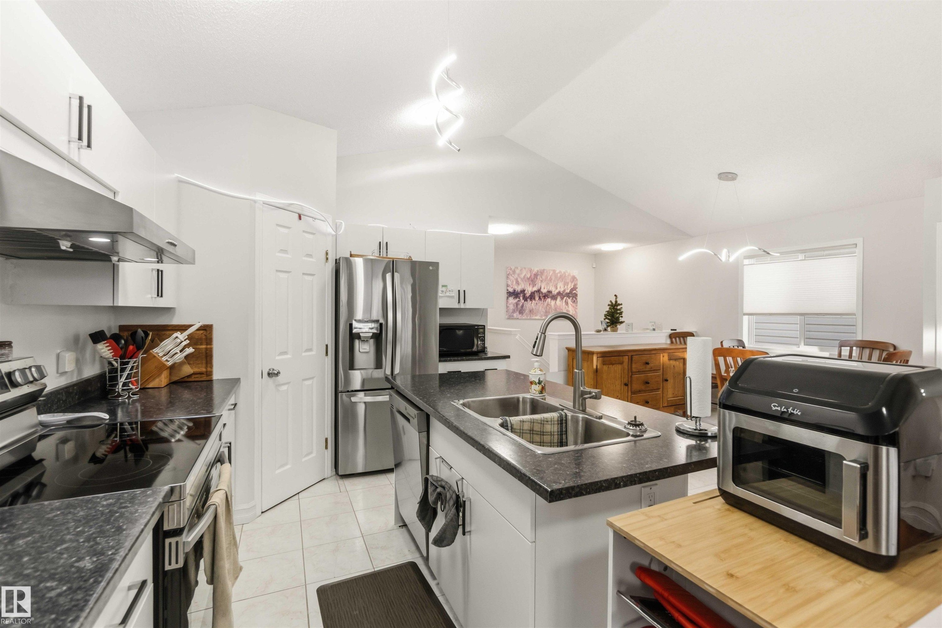 Kitchen featuring stainless steel appliances, white cabinets, vaulted ceiling, light tile patterned floors, and an island with sink - 1706 Turvey Bend, Edmonton, AB - Indoor Photo Showing Kitchen With Stainless Steel Kitchen With Double Sink With Upgraded Kitchen
