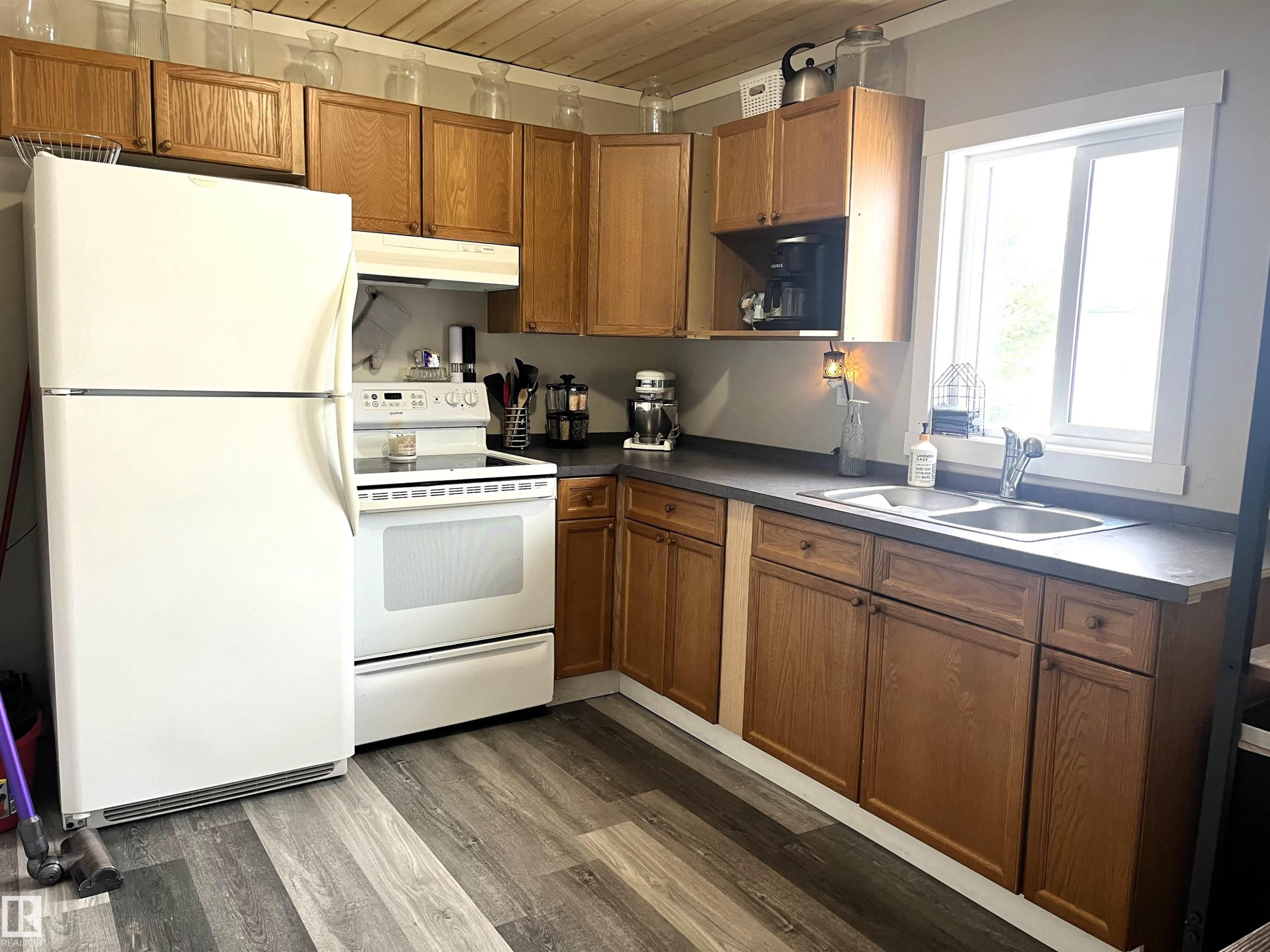 Kitchen featuring wood finish cabinets, white appliances, dark wood-style flooring, dark countertops, and wood ceiling - 4811 48 Ave, Evansburg, AB - Indoor Photo Showing Kitchen With Double Sink