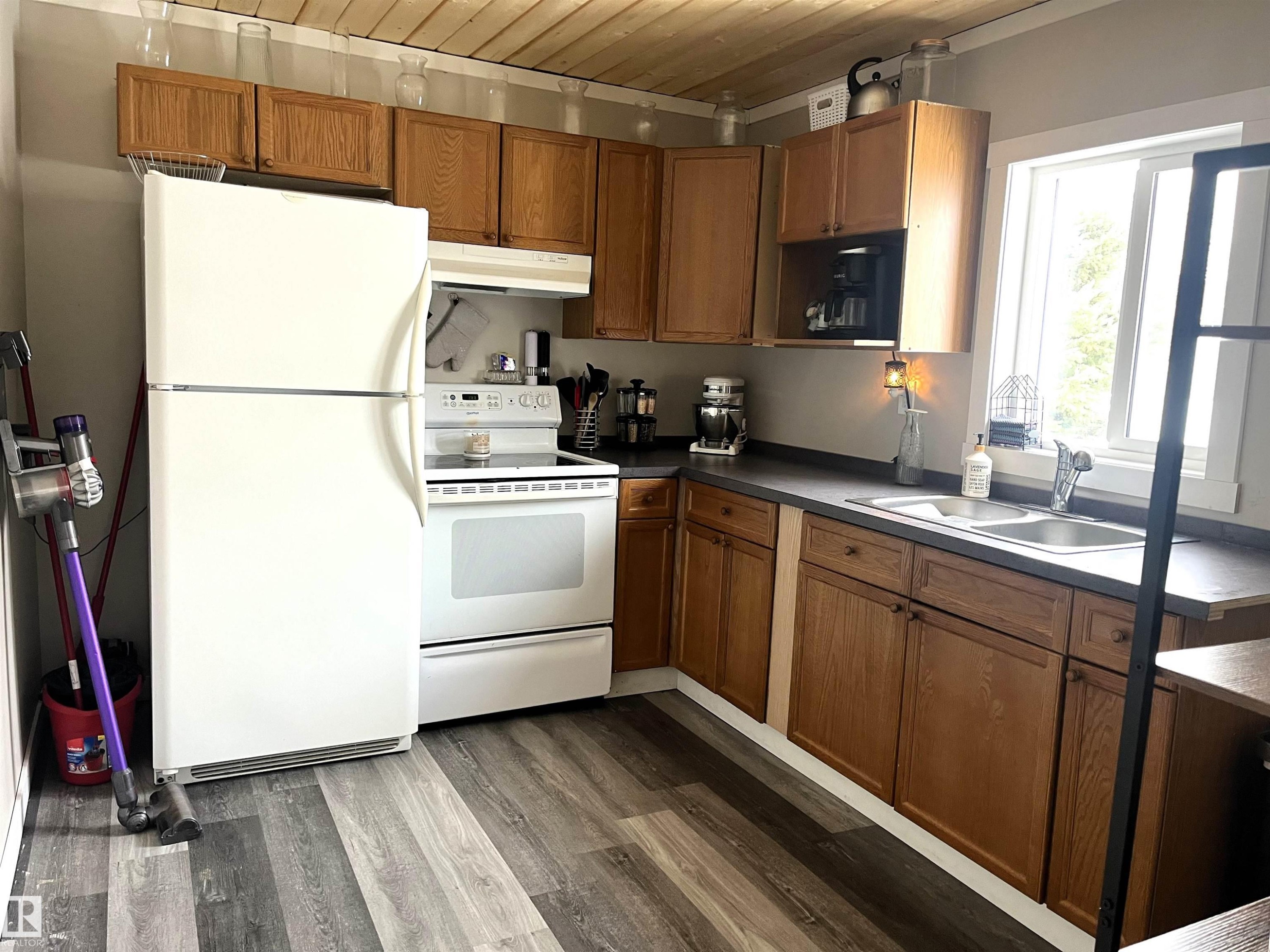 Kitchen featuring white appliances, wood finish cabinetry, dark wood-style flooring, wood ceiling, and dark countertops - 4811 48 Ave, Evansburg, AB - Indoor Photo Showing Kitchen With Double Sink
