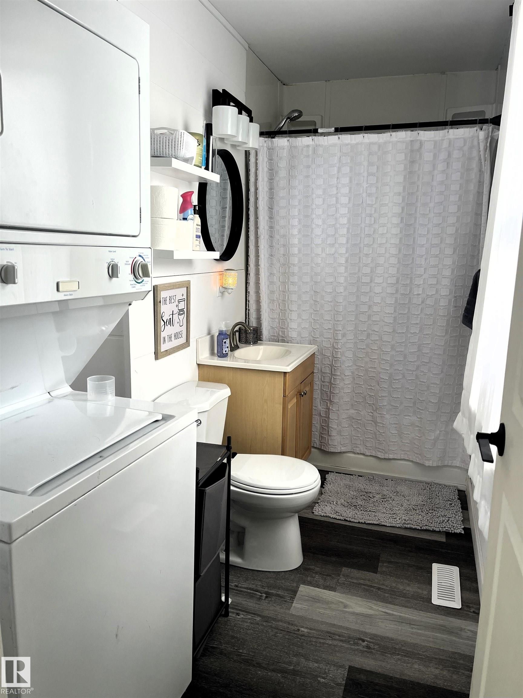 Bathroom with vanity, dark wood-style floors, shower / bath combination with curtain, and stacked washer / drying machine - 4811 48 Ave, Evansburg, AB - Indoor