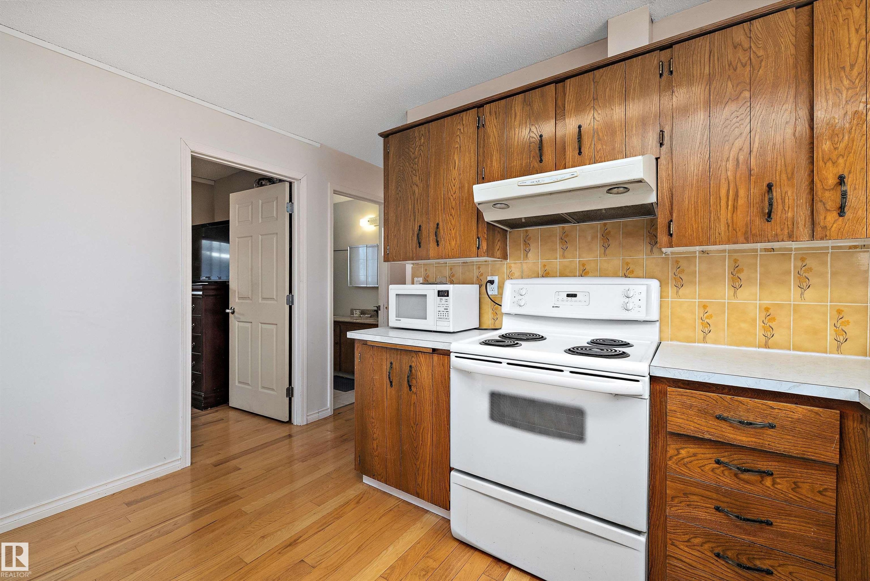 Kitchen featuring white appliances, light countertops, wood finish cabinetry, light wood-type flooring, and a textured ceiling - 12117 91 Street, Edmonton, AB - Indoor Photo Showing Kitchen