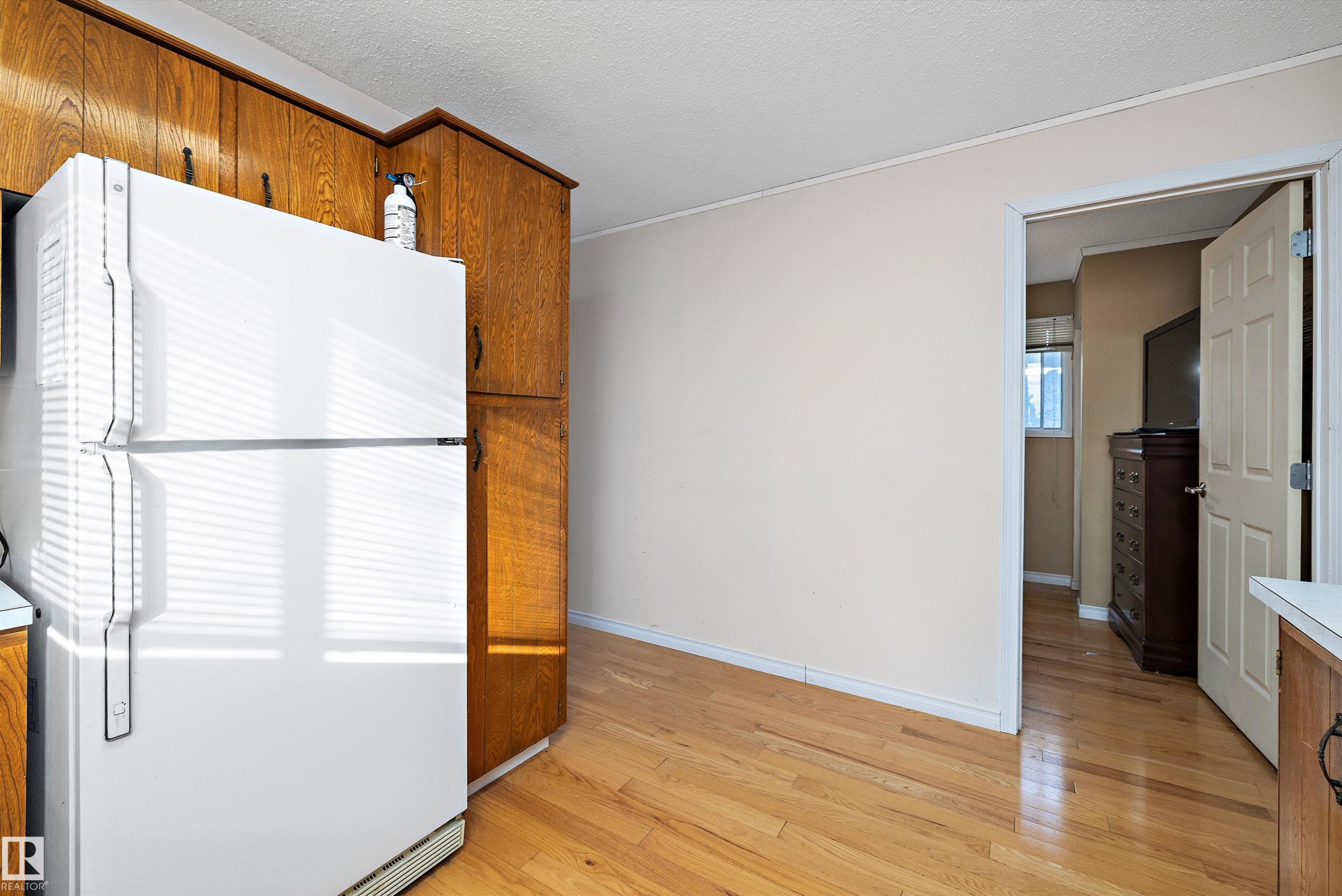 Kitchen with freestanding refrigerator, wood finish cabinetry, light wood-style flooring, a textured ceiling, and light countertops - 12117 91 Street, Edmonton, AB - Indoor Photo Showing Other Room