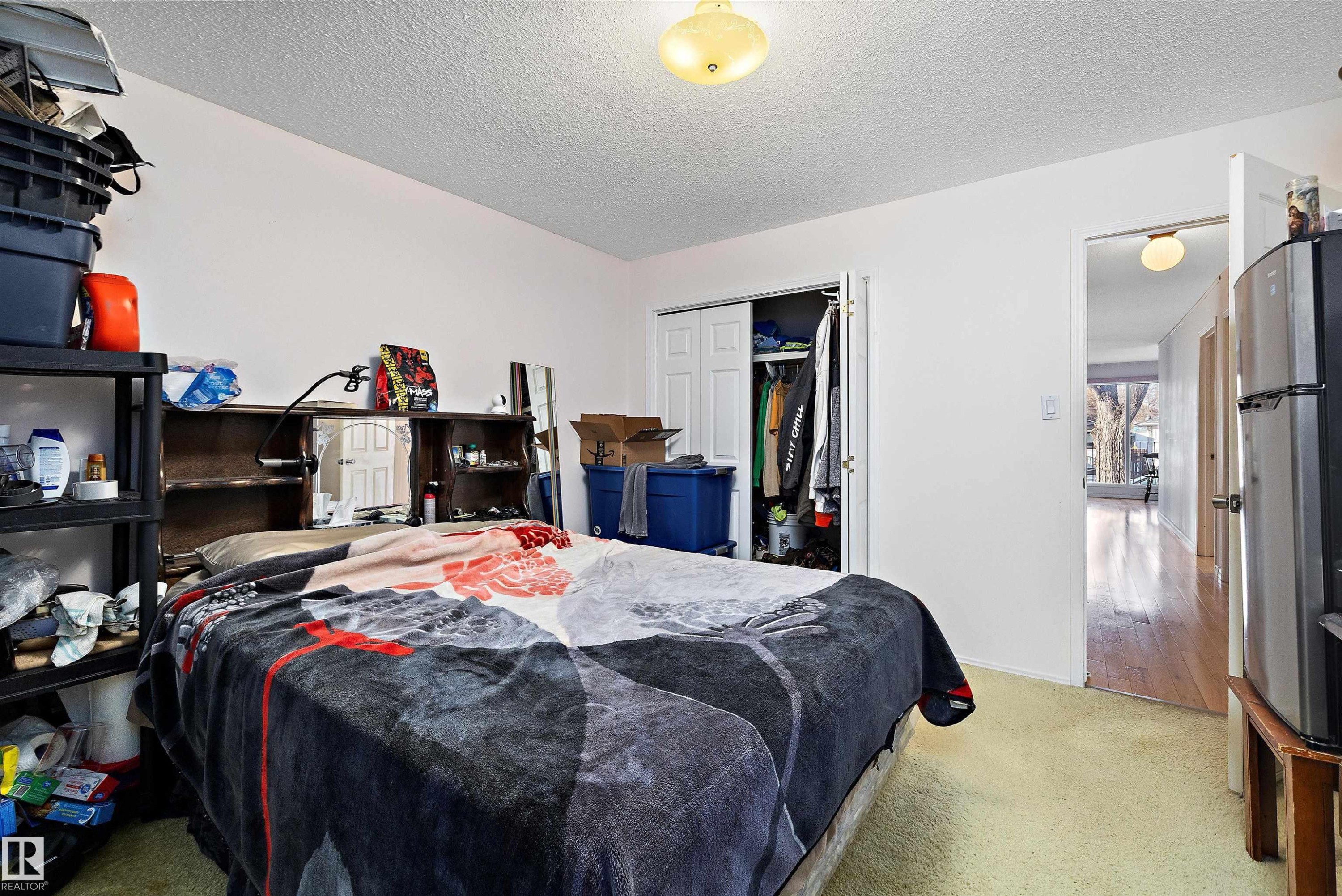 Carpeted bedroom featuring freestanding refrigerator, a textured ceiling, and a closet - 12117 91 Street, Edmonton, AB - Indoor Photo Showing Bedroom