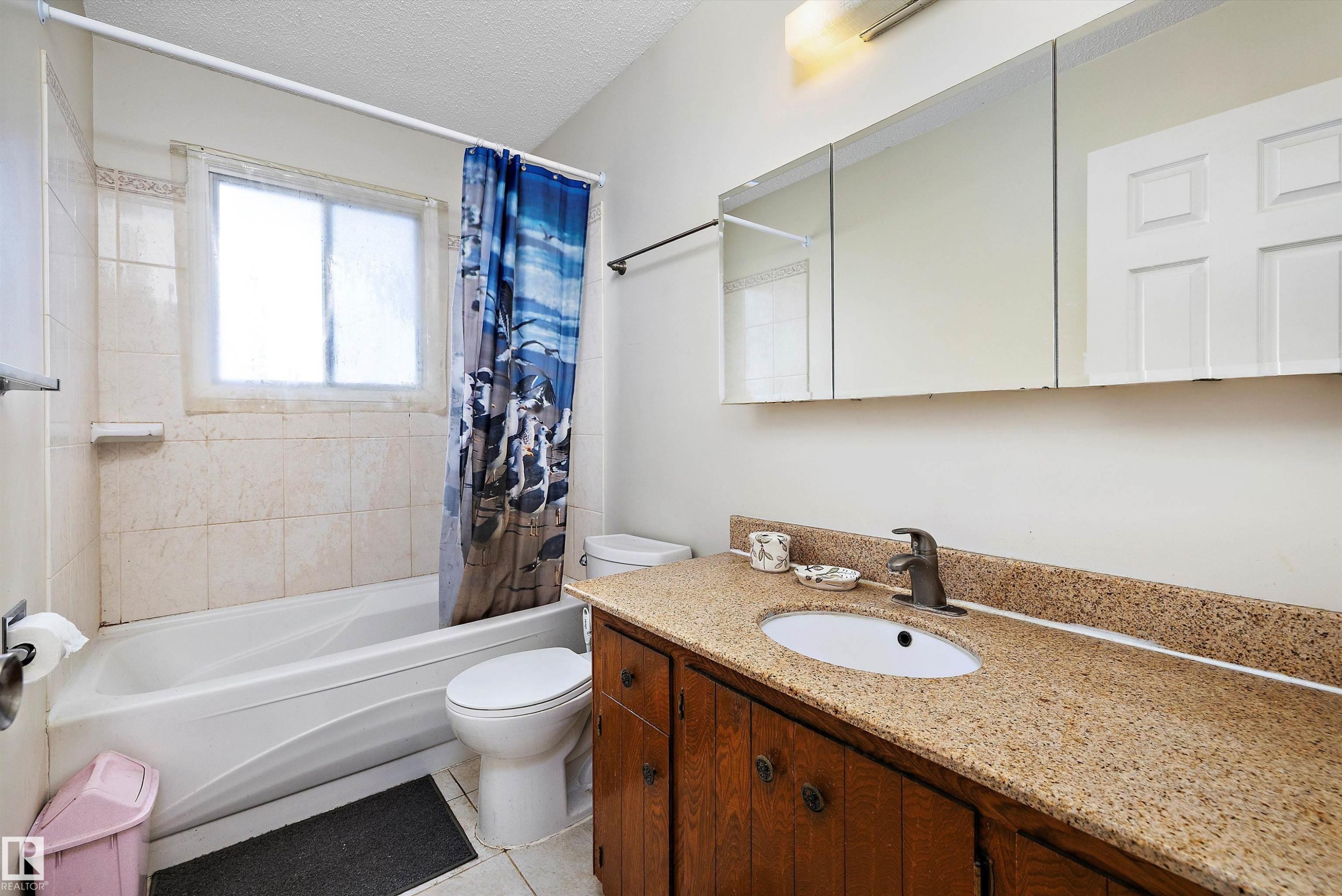 Full bath featuring vanity, shower / bath combo with shower curtain, a textured ceiling, and light tile patterned flooring - 12117 91 Street, Edmonton, AB - Indoor Photo Showing Bathroom