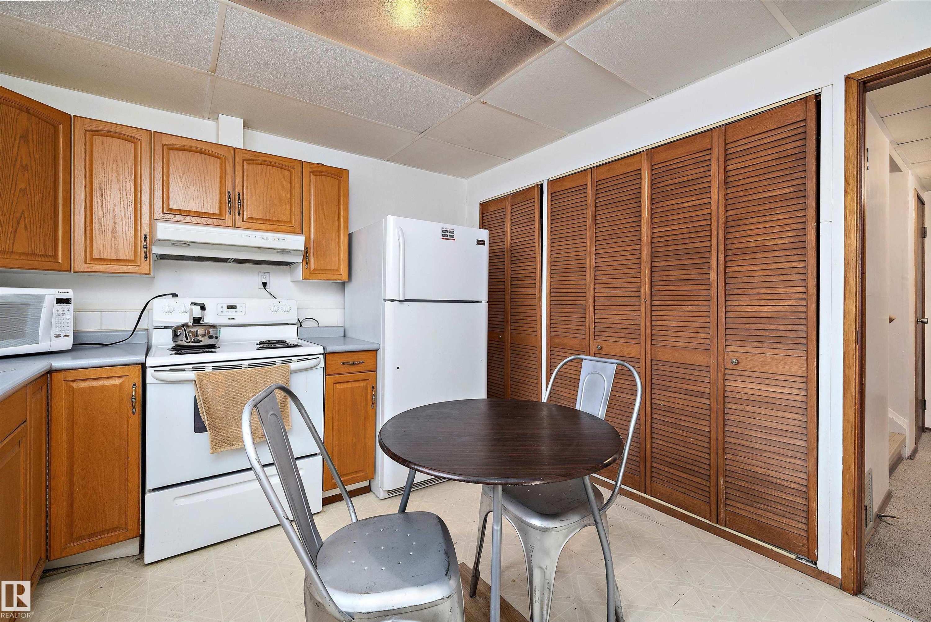Kitchen featuring light floors, white appliances, wood finish cabinetry, and a drop ceiling - 12117 91 Street, Edmonton, AB - Indoor Photo Showing Kitchen